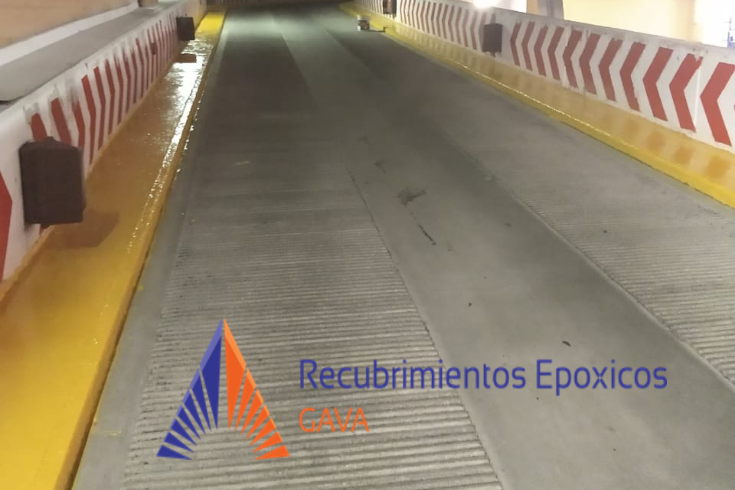 Entrada de un túnel con barreras de protección amarillas y marcas de señalización en las paredes. Hay una marca de agua con el texto "Recubrimientos Epóxicos Gava".