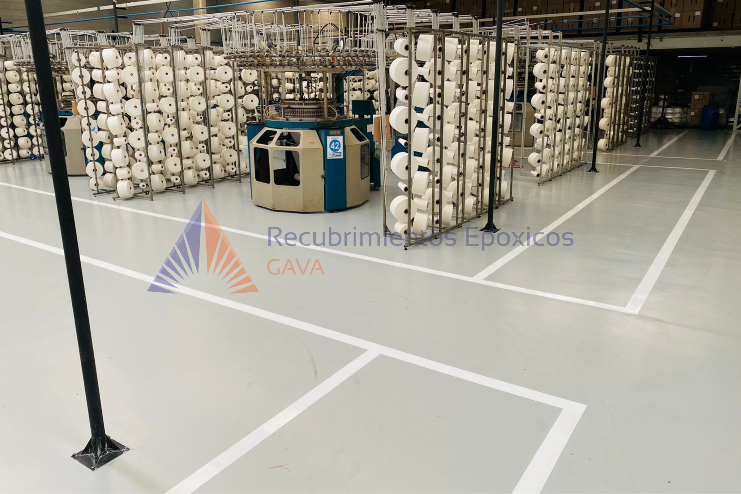 Área de producción textil con máquinas de hilado y bobinas de hilo blancas, en un ambiente industrial.