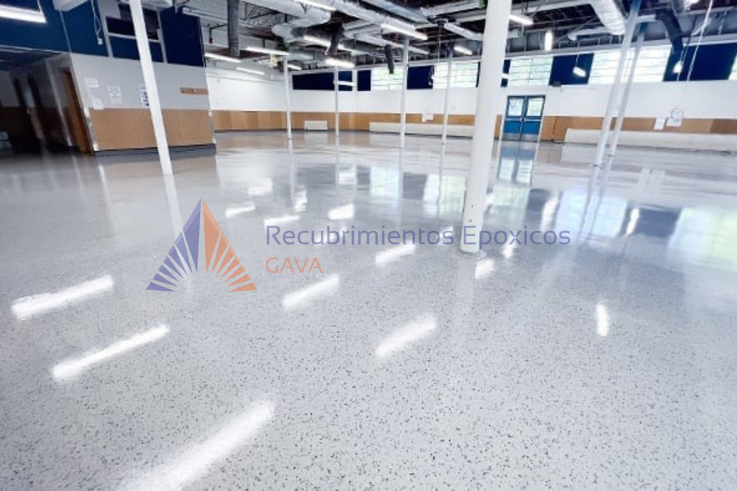 Interior de un gimnasio con suelo brillante de epoxi, paredes blancas y ventanales grandes. Se observa el logotipo de Recubrimientos Epóxicos GAVA en la parte inferior izquierda.