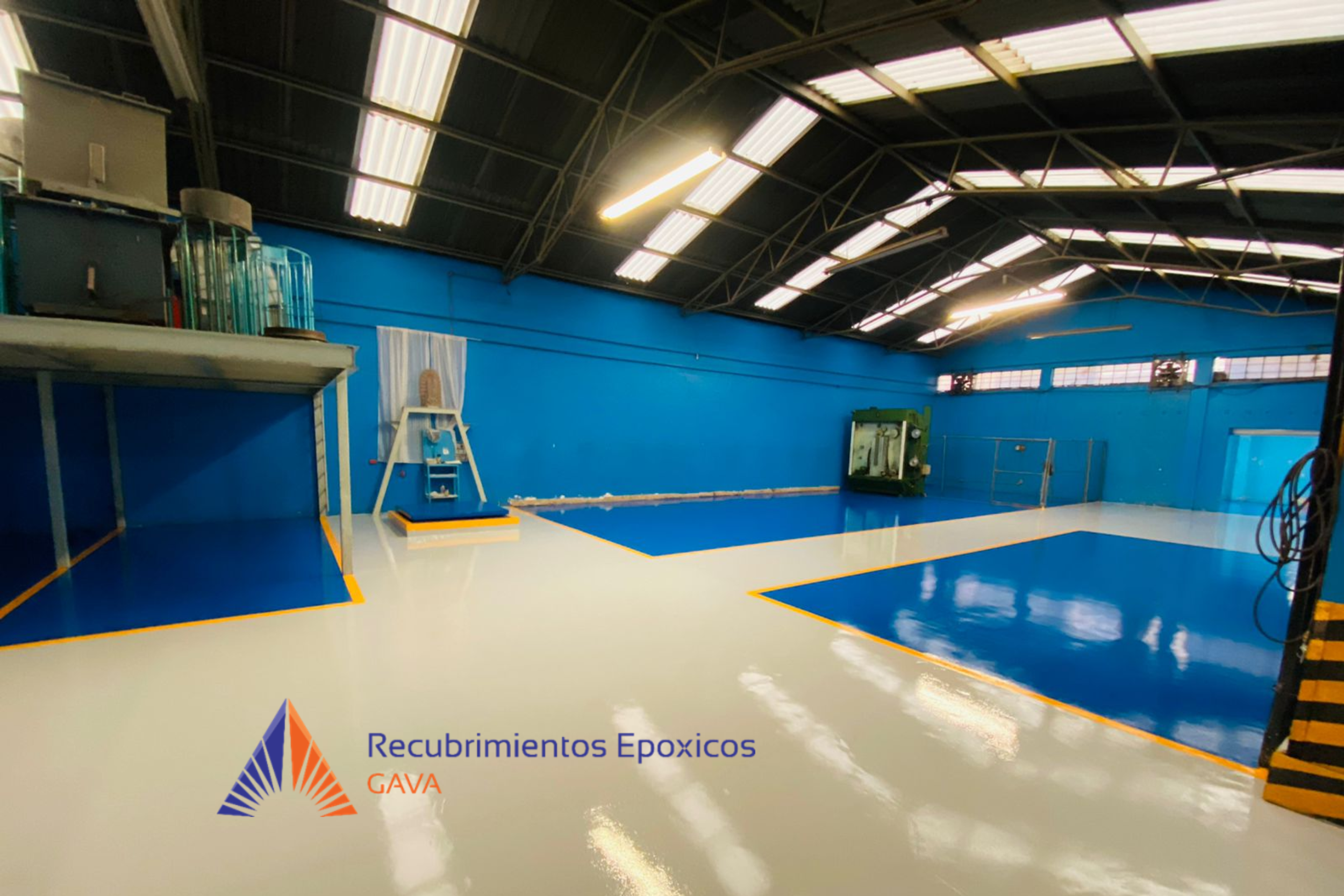 Vista de un interior de una cancha deportiva con paredes azules, piso blanco con línea amarilla, y un logo que dice "Recubrimientos Epóxicos GAVA" en la esquina inferior izquierda.