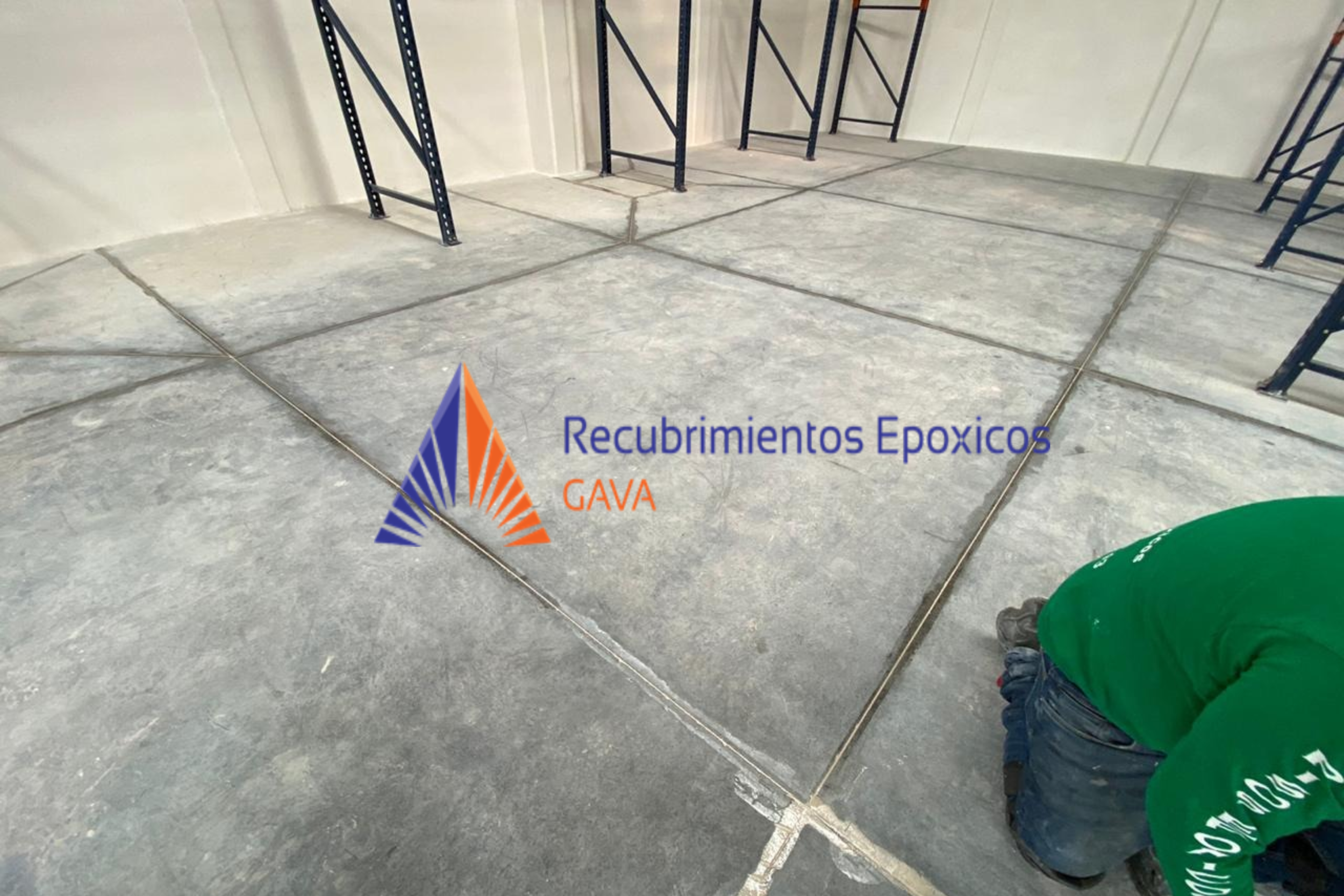 Imagen de un espacio en construcción con baldosas de cemento y estanterías metálicas, y un trabajador en posición agachada usando un uniforme verde y botas negras. En primer plano, el logo y texto en color azul y naranja "Recubrimientos Epóxicos GAVA