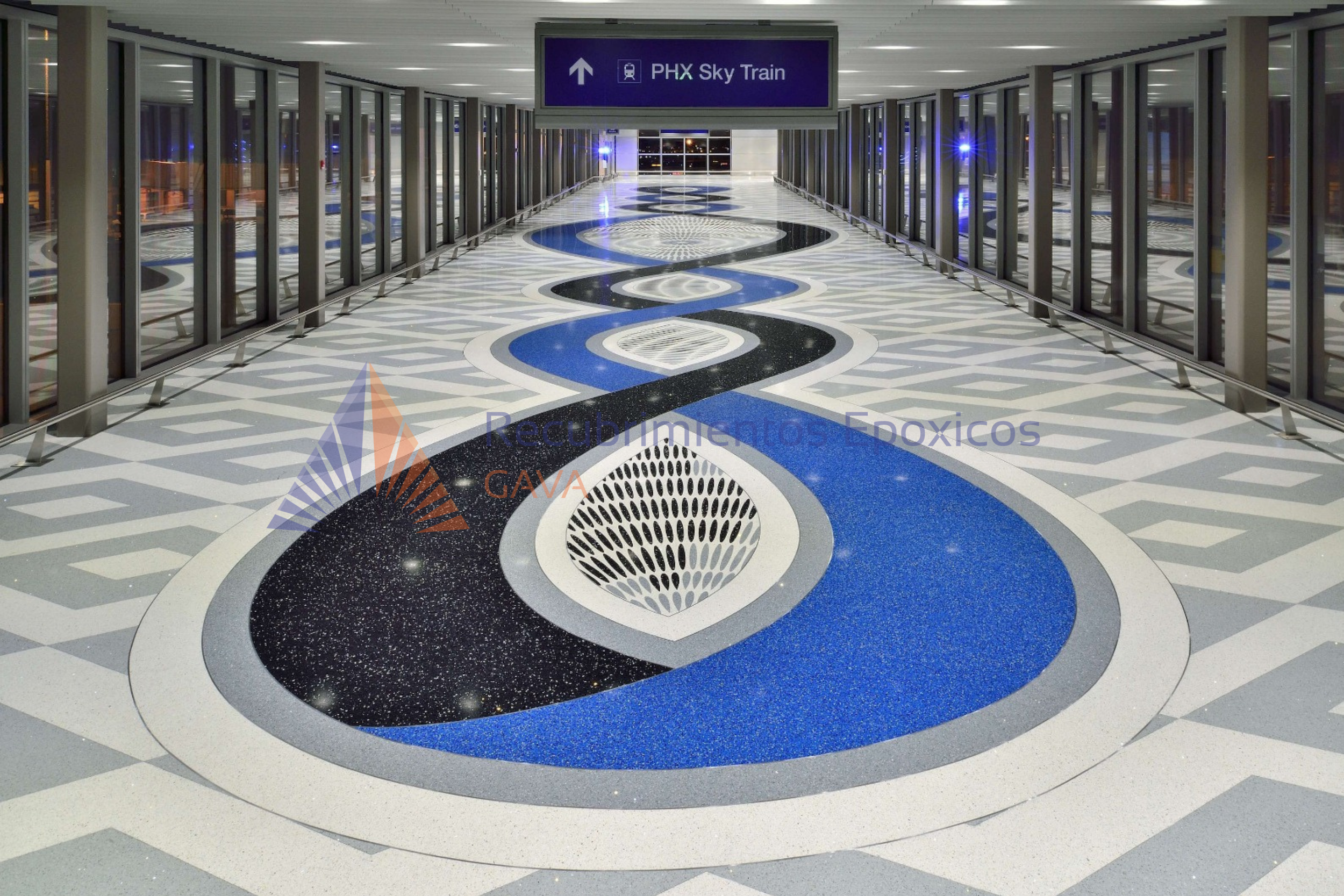 Pasillo del aeropuerto con señal que indica direccion al tren Skylight de Phoenix, suelo decorado con patrones de círculos en colores azul, negro y gris, paredes con ventanas.