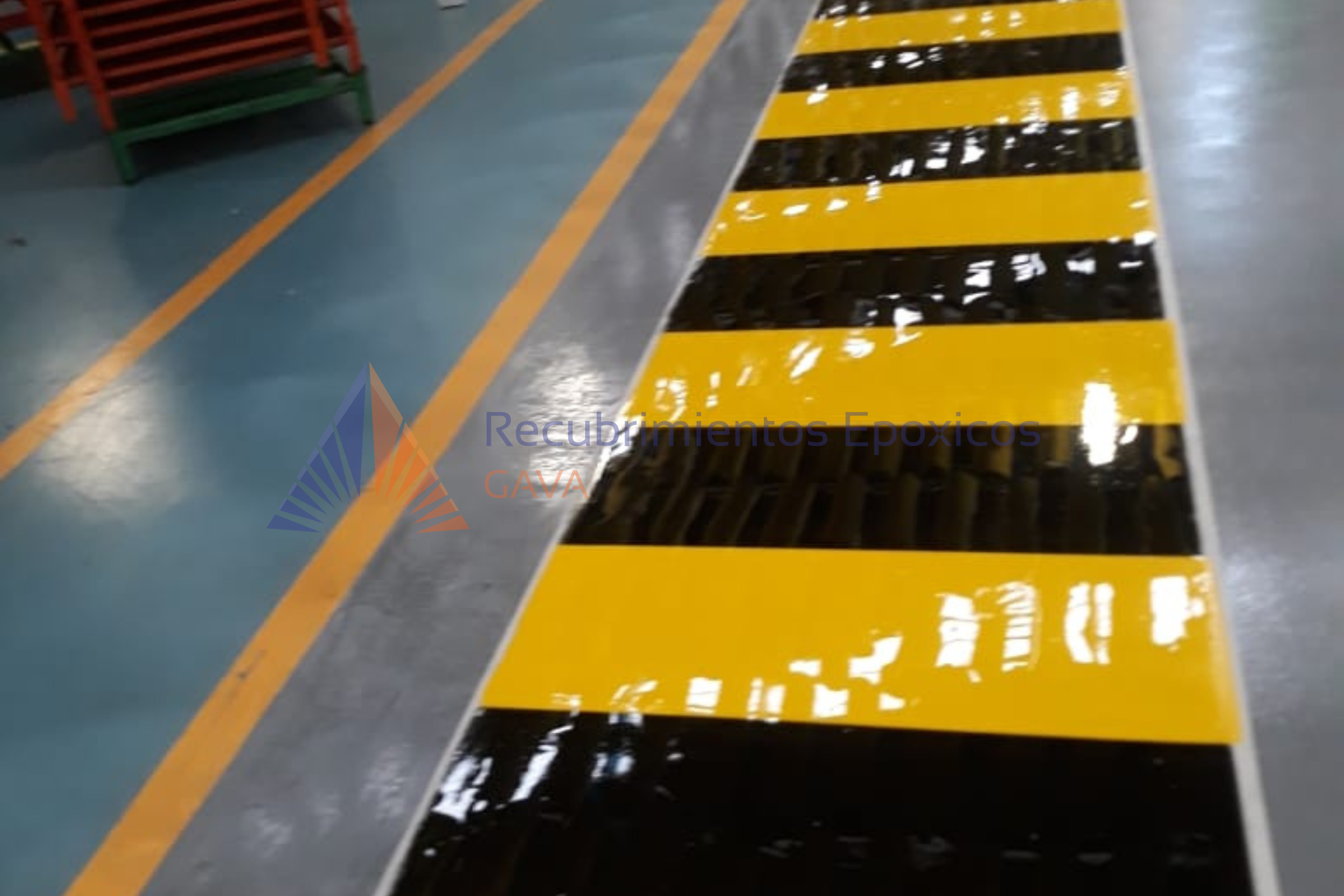 Suelo de una zona industrial o de un taller con bandas de advertencia amarillas y negras, y líneas amarillas en el piso.