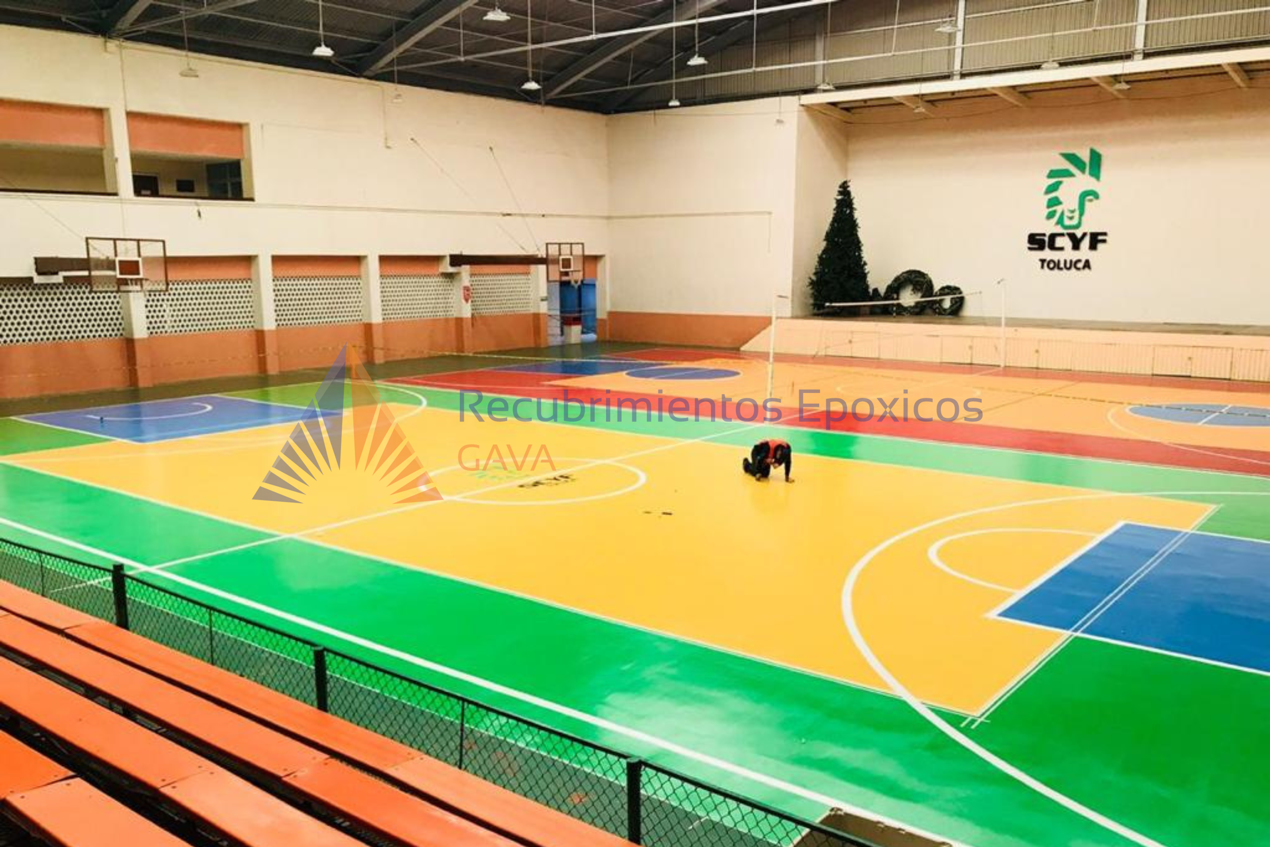 Pista de baloncesto y voleibol en un gimnasio cubierto con paredes beige y techo de metal, decorada con un árbol de Navidad y letras que dicen 'SCYF Toluca'.