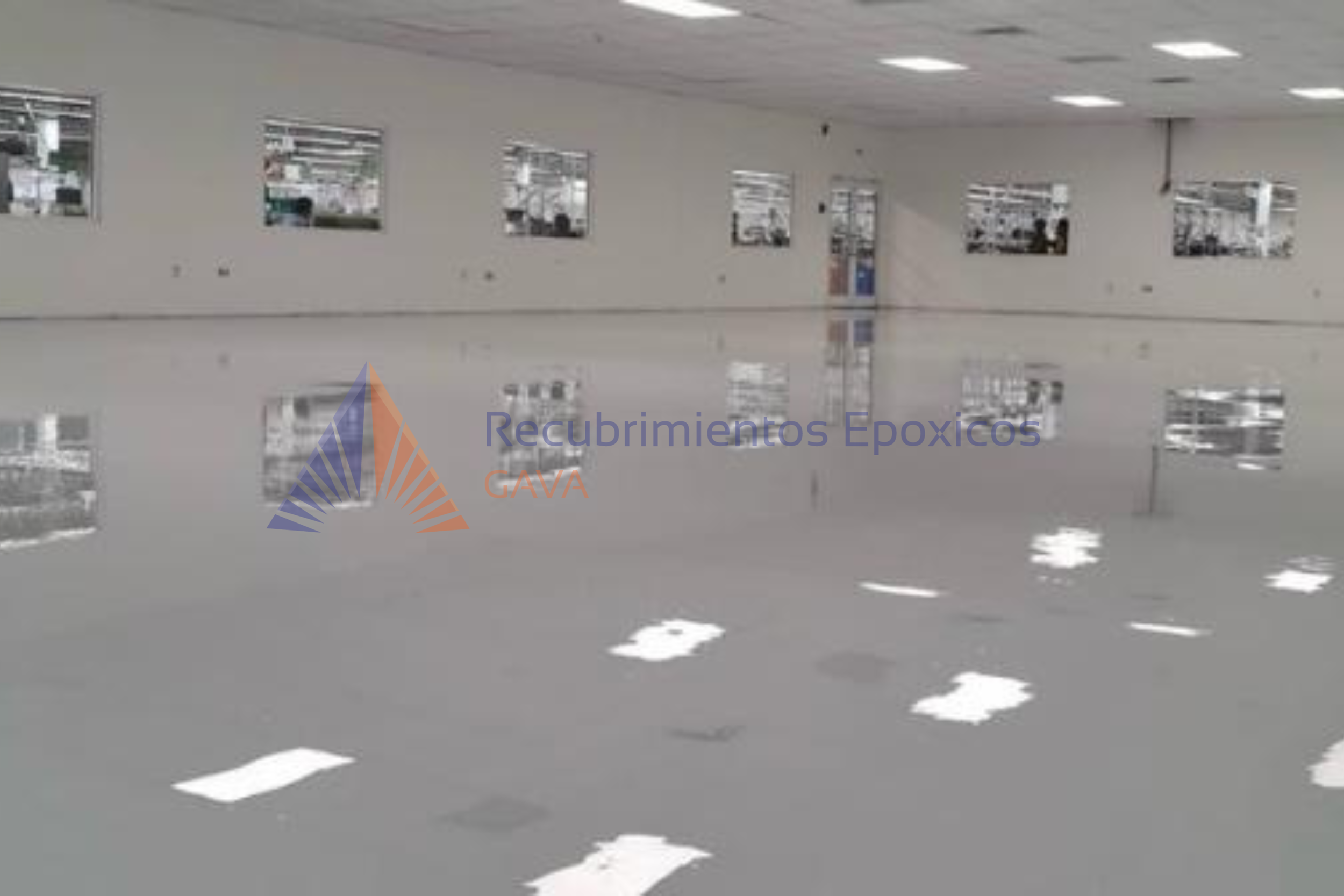Interior de un salón con suelo de color gris y paredes blancas. Ventanas en la pared izquierda y en el fondo que muestran un exterior con vehículos y edificios. Se observa un logo en la esquina inferior izquierda con la leyenda 'Recubrimientos Epóxic