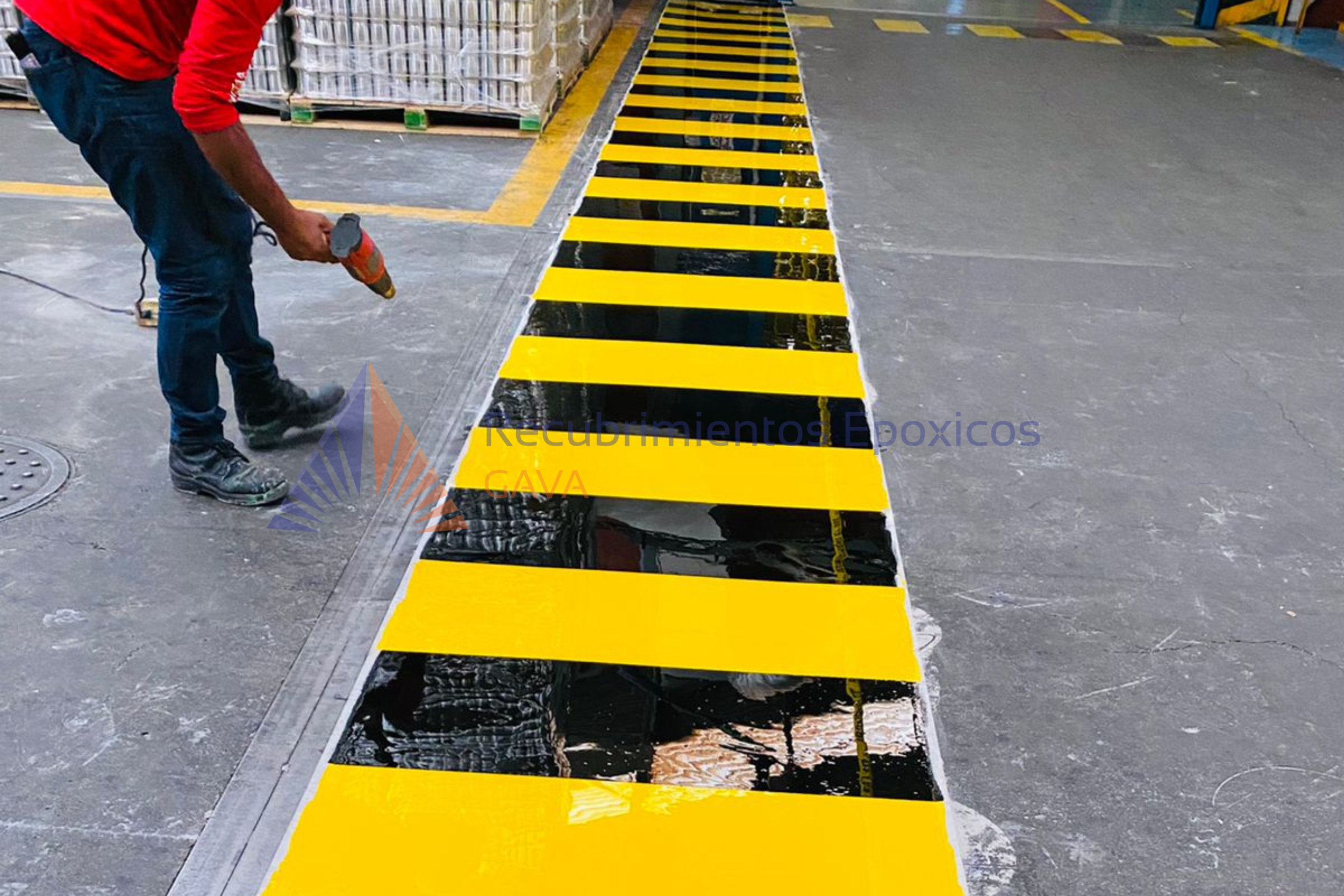 Persona trabajando en señalización de suelo amarillo y negro en un almacén o área industrial.