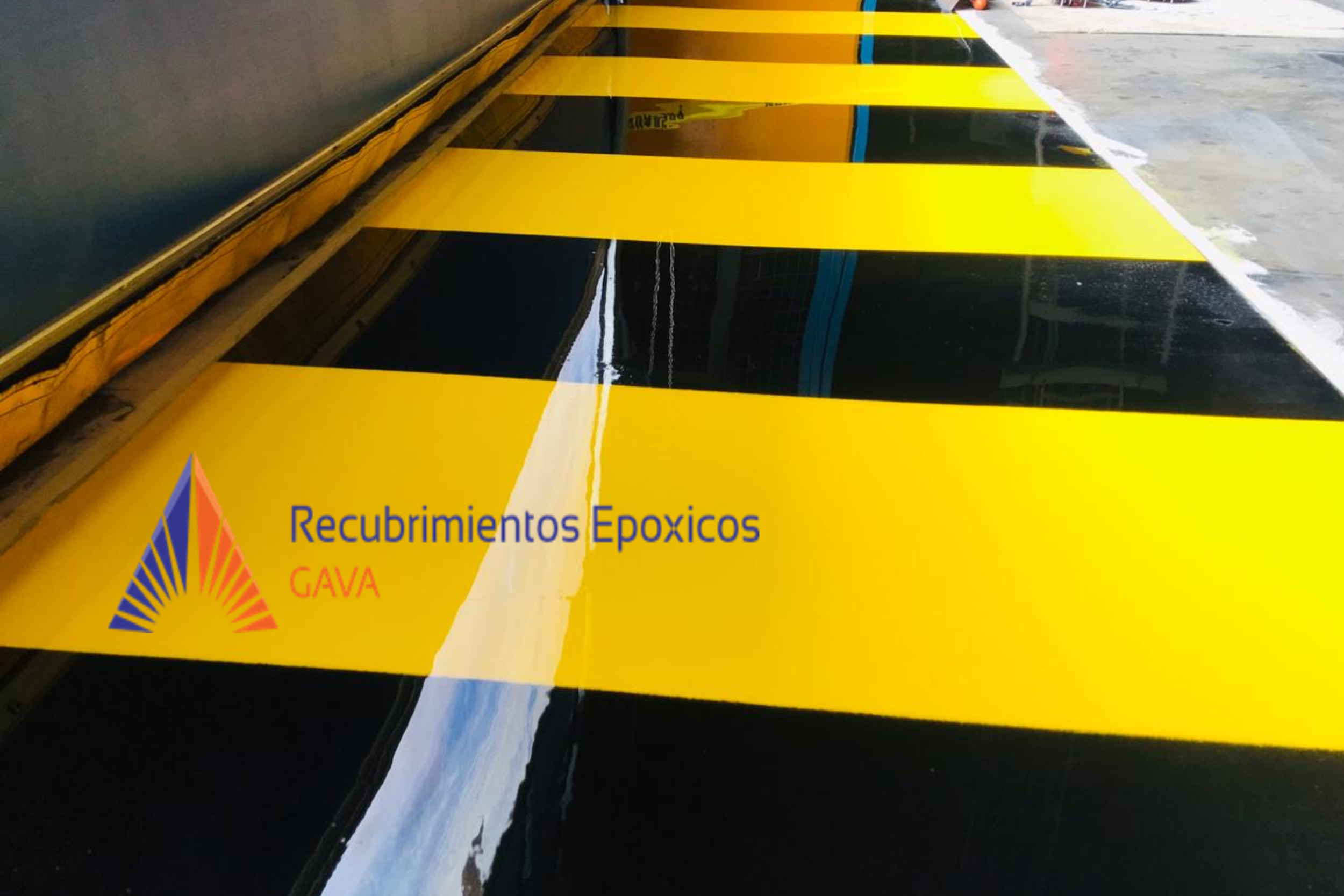 Imagen de una valla de precaución amarilla y negra con texto en español que dice 'Recubrimientos Epóxicos' y un logo con los colores azul, naranja, y morado. La valla parece estar en una superficie de concreto.