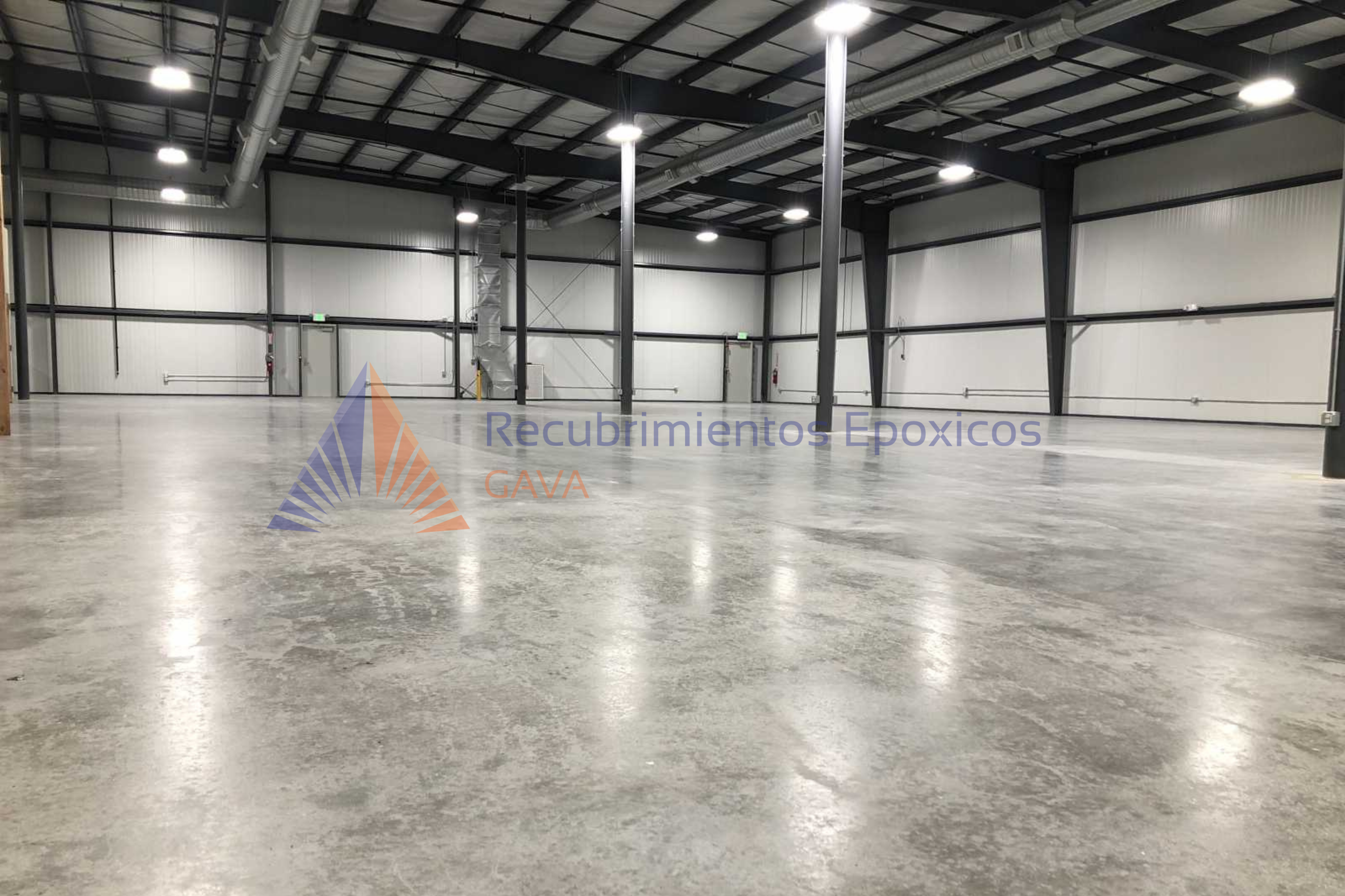 Interior de un almacén o bodega con piso de concreto, paredes de metal y techumbre de estructura de acero con luces empotradas y sistemas de ventilación y ductos visibles.