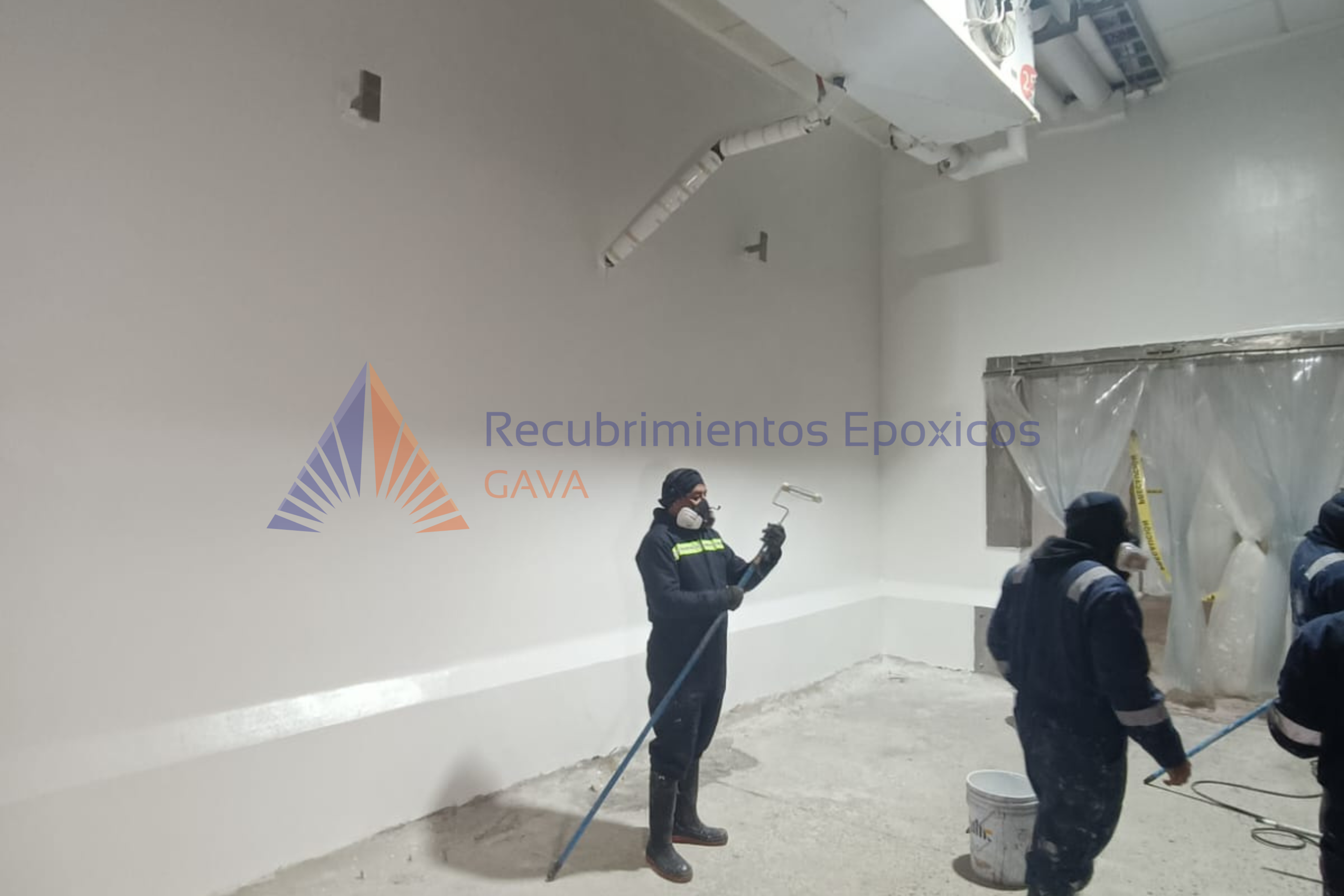 Personas trabajando en una aplicación de recubrimiento epóxico en un espacio interior, usando equipo de protección personal.