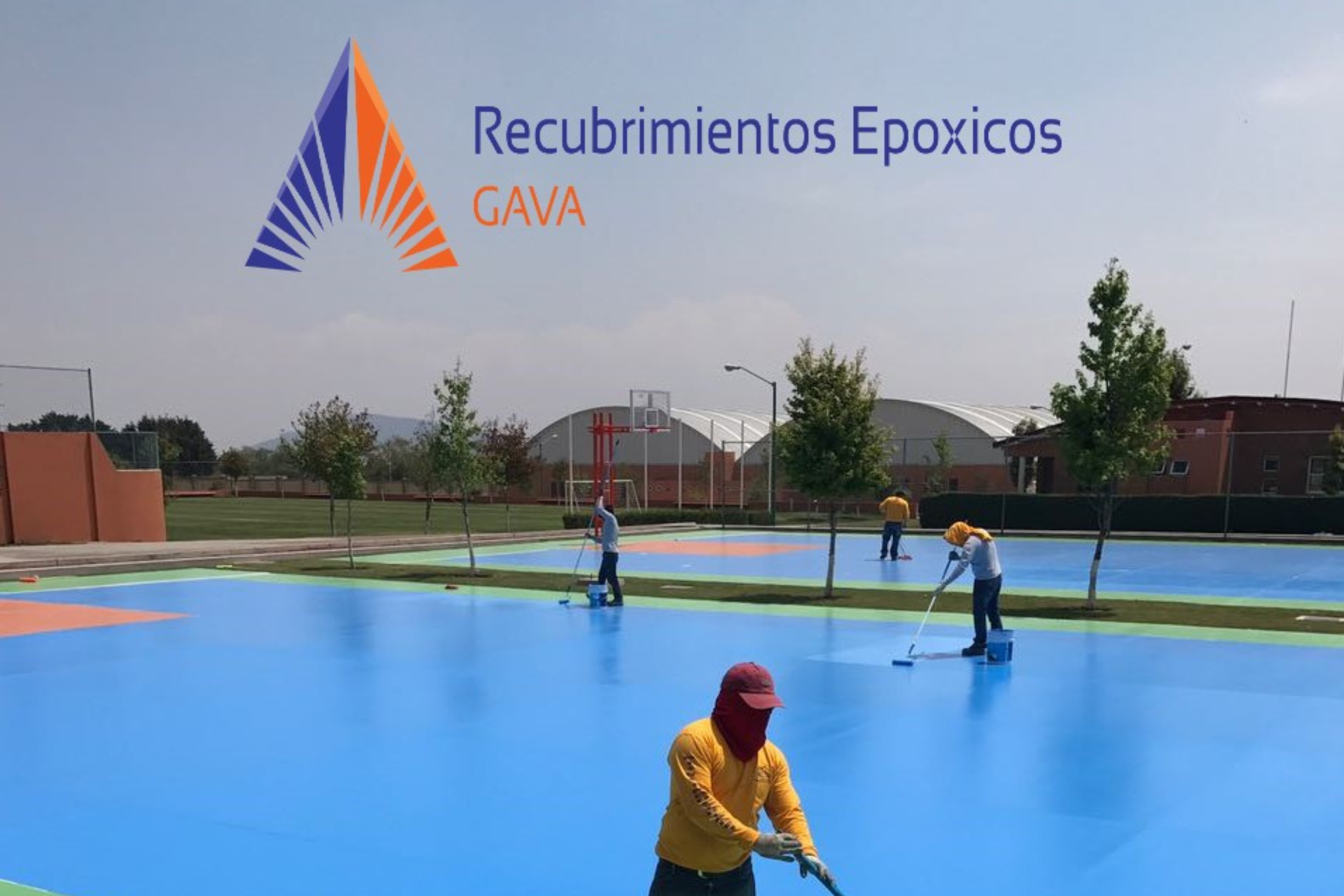 Personas pintando una cancha deportiva con recubrimiento epóxico de color azul y detalles en naranja, en un área al aire libre con árboles y estructuras deportivas a su alrededor.