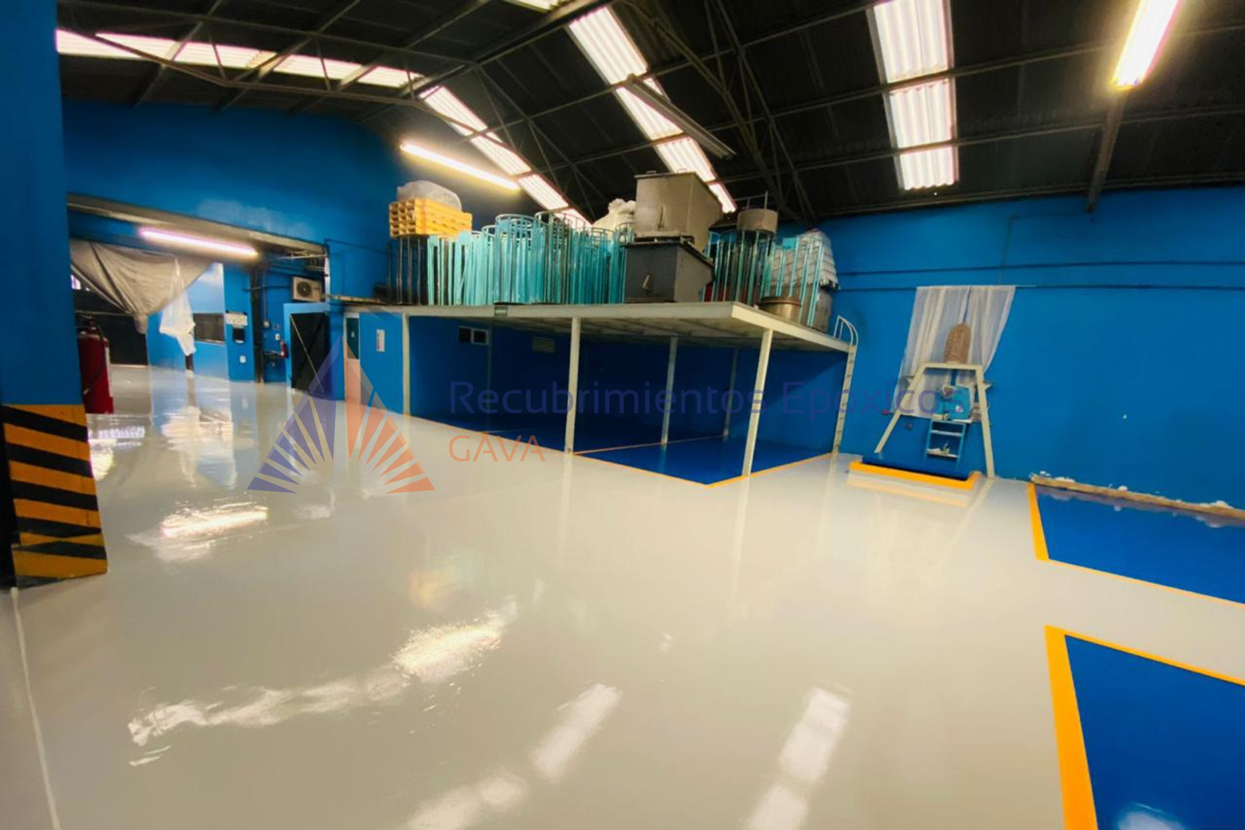 Interiores de una fábrica con piso liso y paredes azules, con herramientas y equipos de trabajo y un área para tareas específicas.