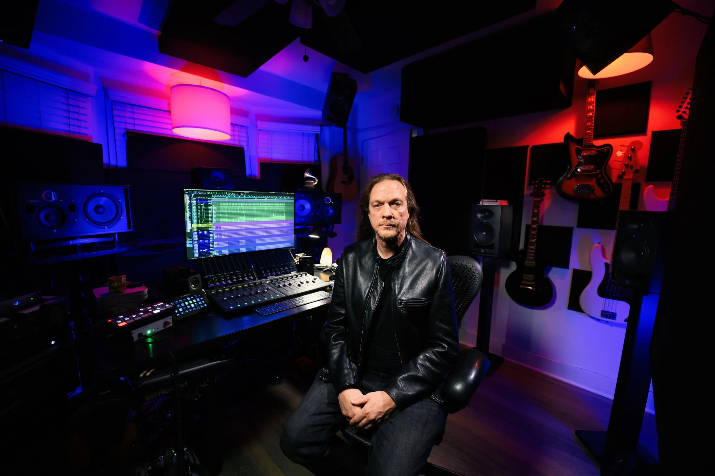 Long haired man sitting in a Dolby Atmos mixing studio with guitars on the wall