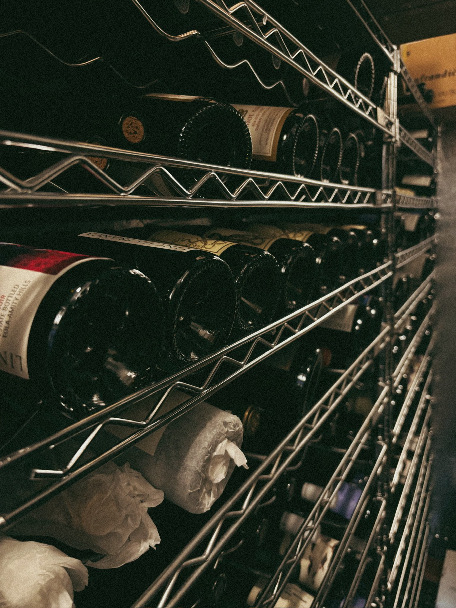 Wine bottles stored in a metal rack, some wrapped in paper.