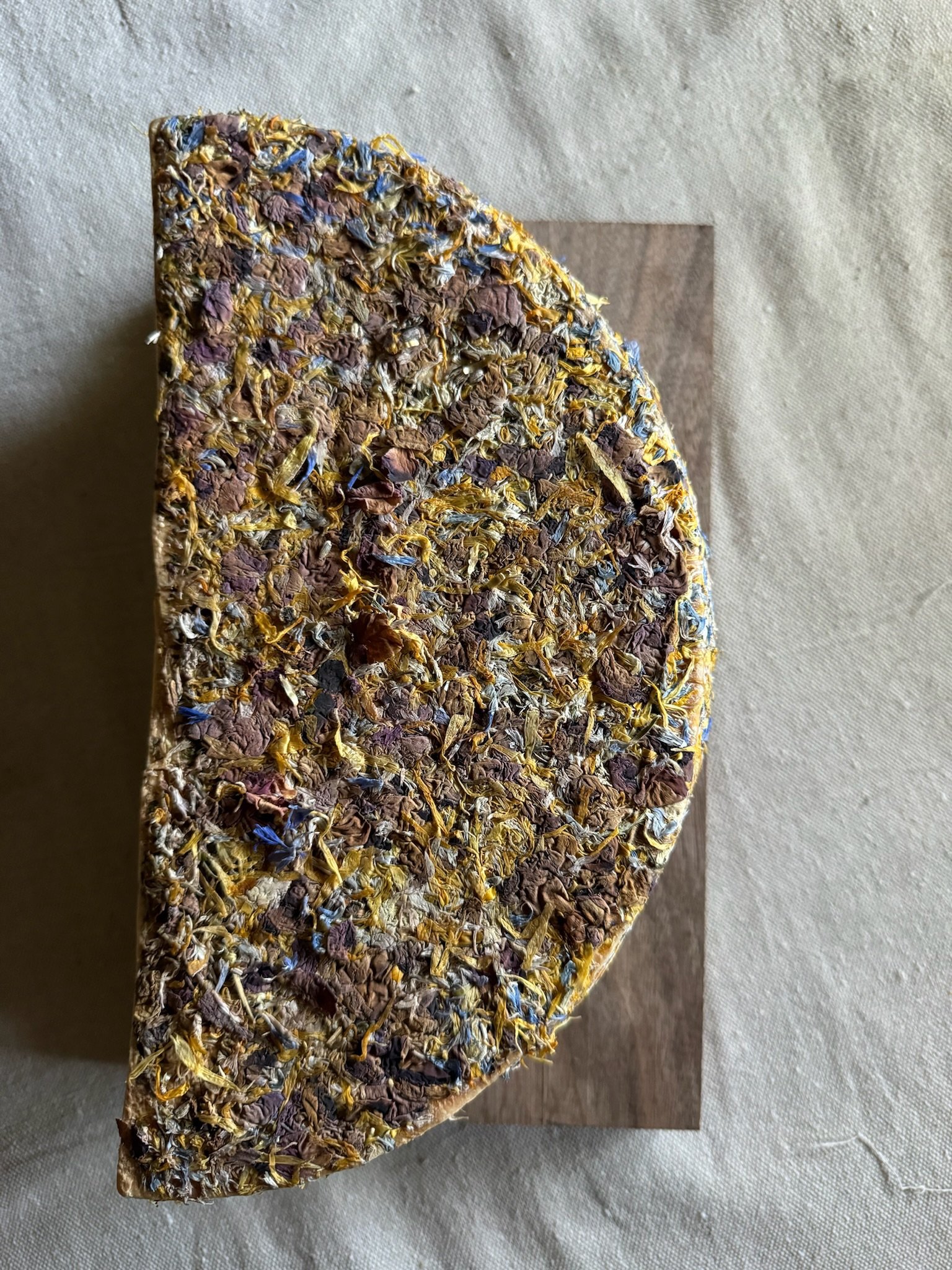 Half wheel of cheese covered with edible flowers on a wooden board