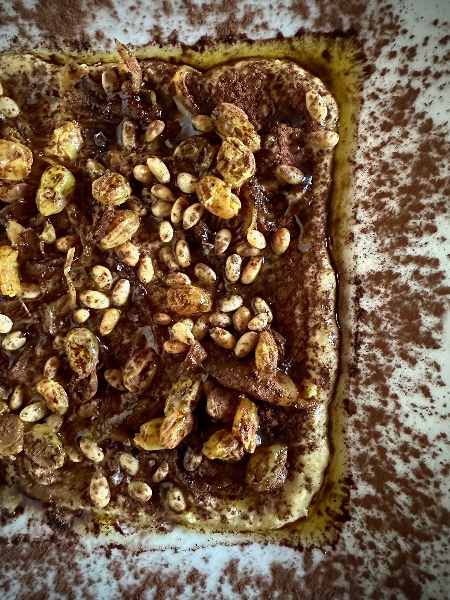 Close-up of a dish featuring hummus with roasted cauliflower, pine nuts, and spices in a decorative presentation.