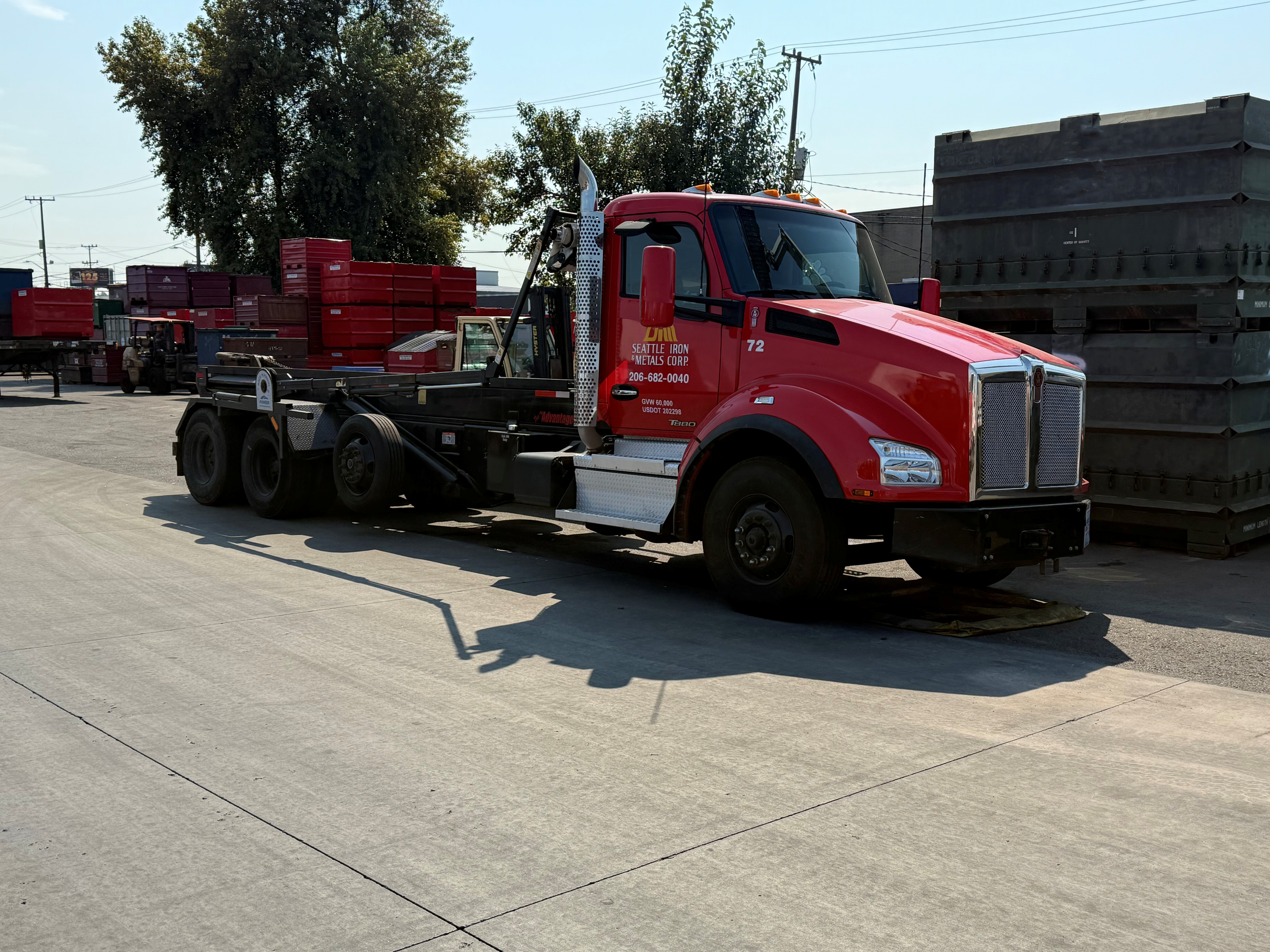 Red semi-truck parked next to stacks of black and red containers on an industrial lot