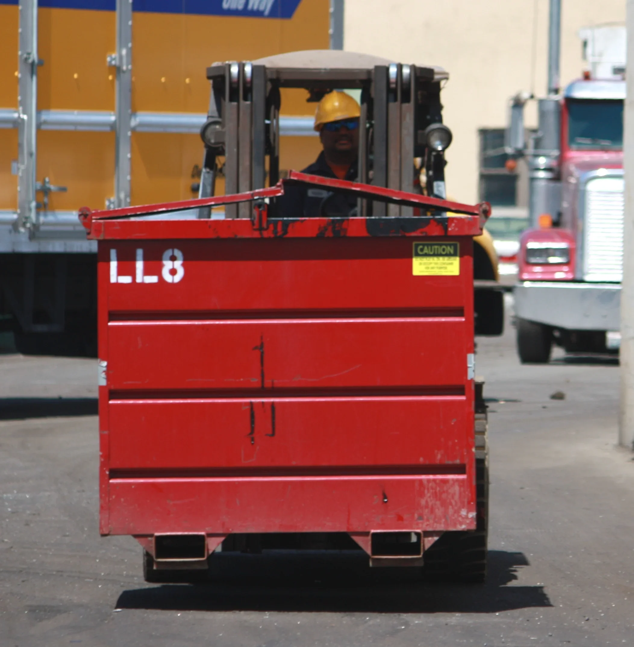 A construction worker wearing a yellow safety helmet and sunglasses operating a red forklift in a construction area.