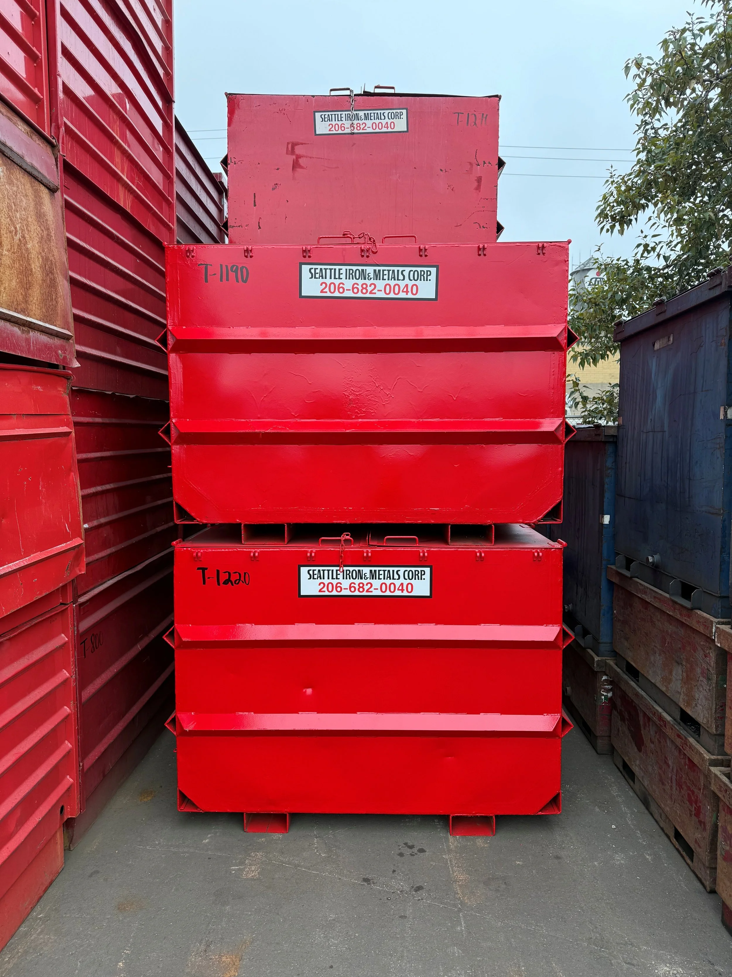 Three red metal shipping containers stacked on top of each other, with labels from Seattle Iron & Metals Corp and contact number 206-682-0040.
