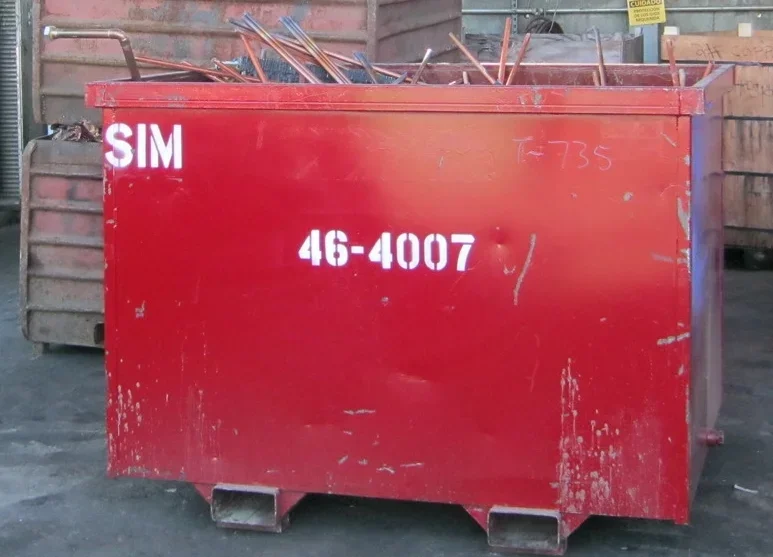 Red dumpster with the number 46-4007 painted on it, contents include metal rods or tools sticking out from the top.