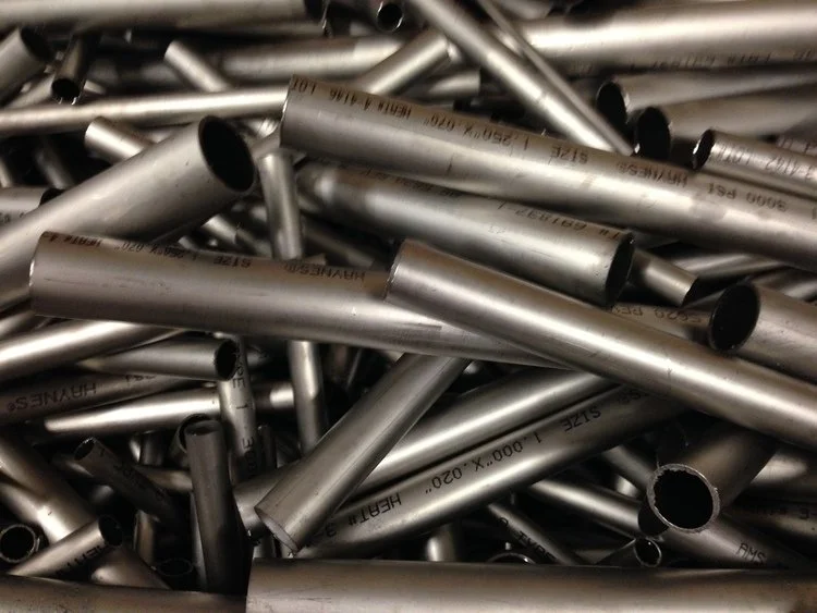 A pile of metal pipes and tubes, some with black interior openings, in various lengths and diameters.