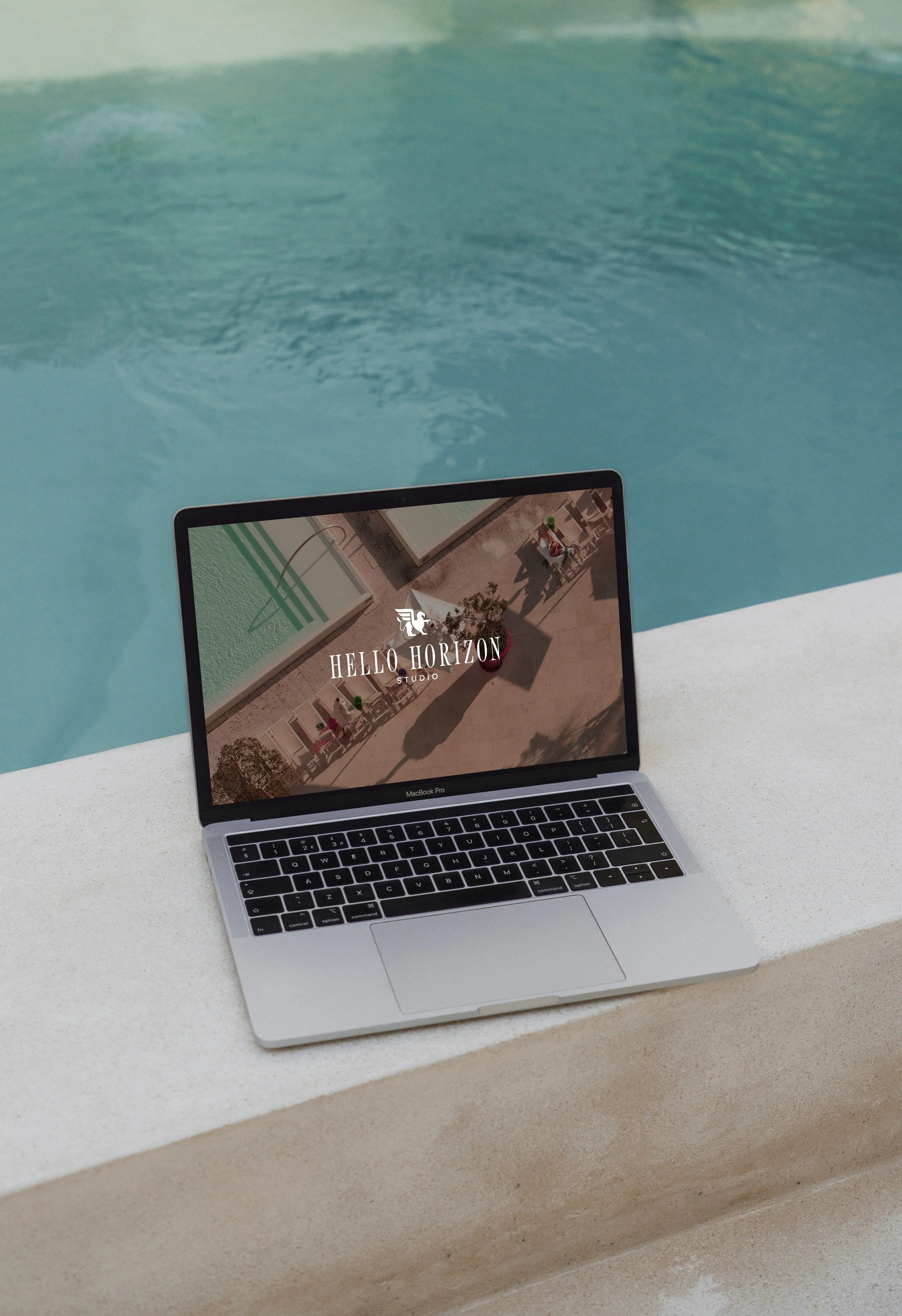 MacBook displaying a small business branding website redesign for a creative studio, set beside a bright blue pool.