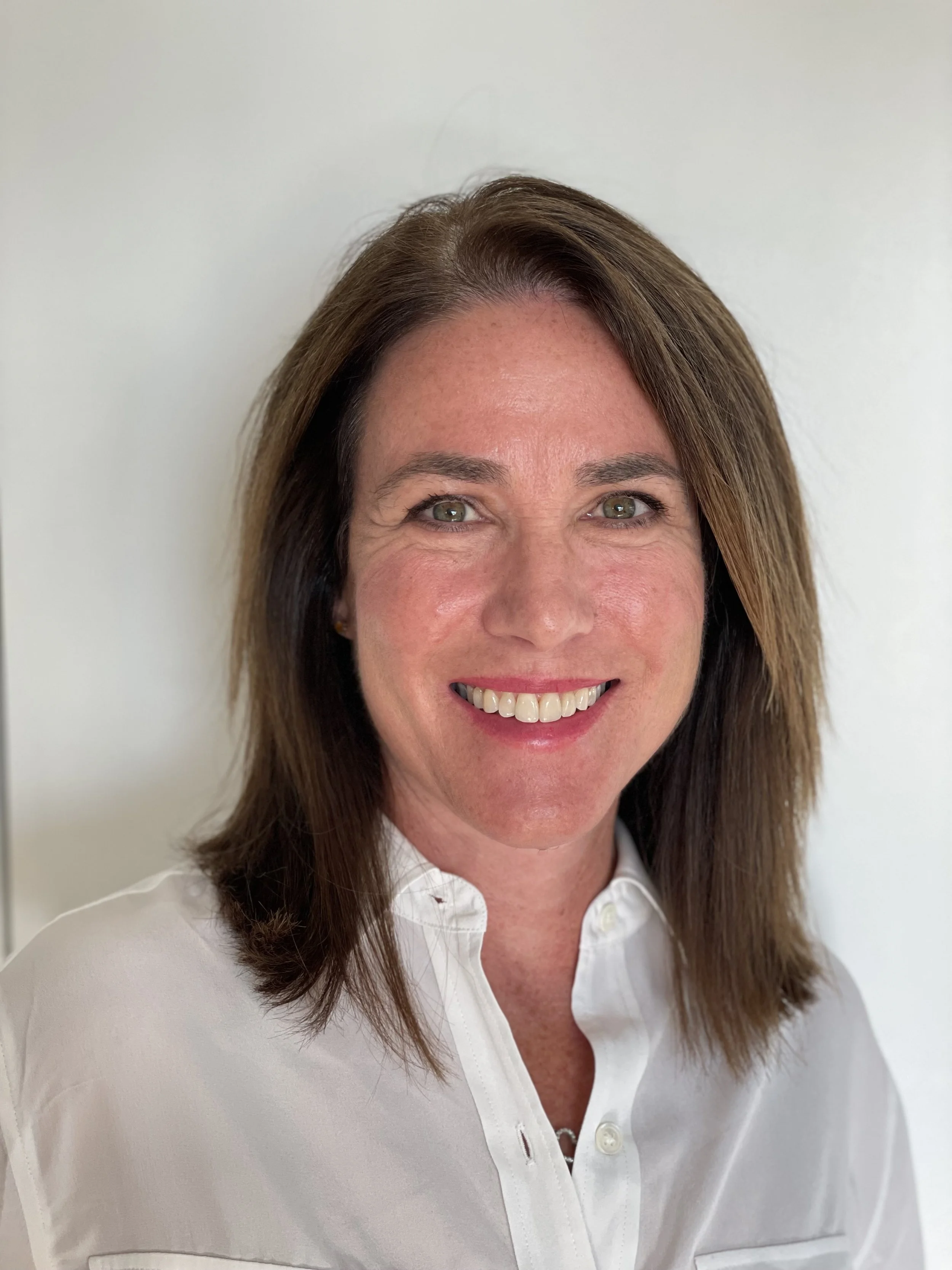 headshot of a woman with shoulder-length, straight, brown hair wearing a white collared shirt and smiling