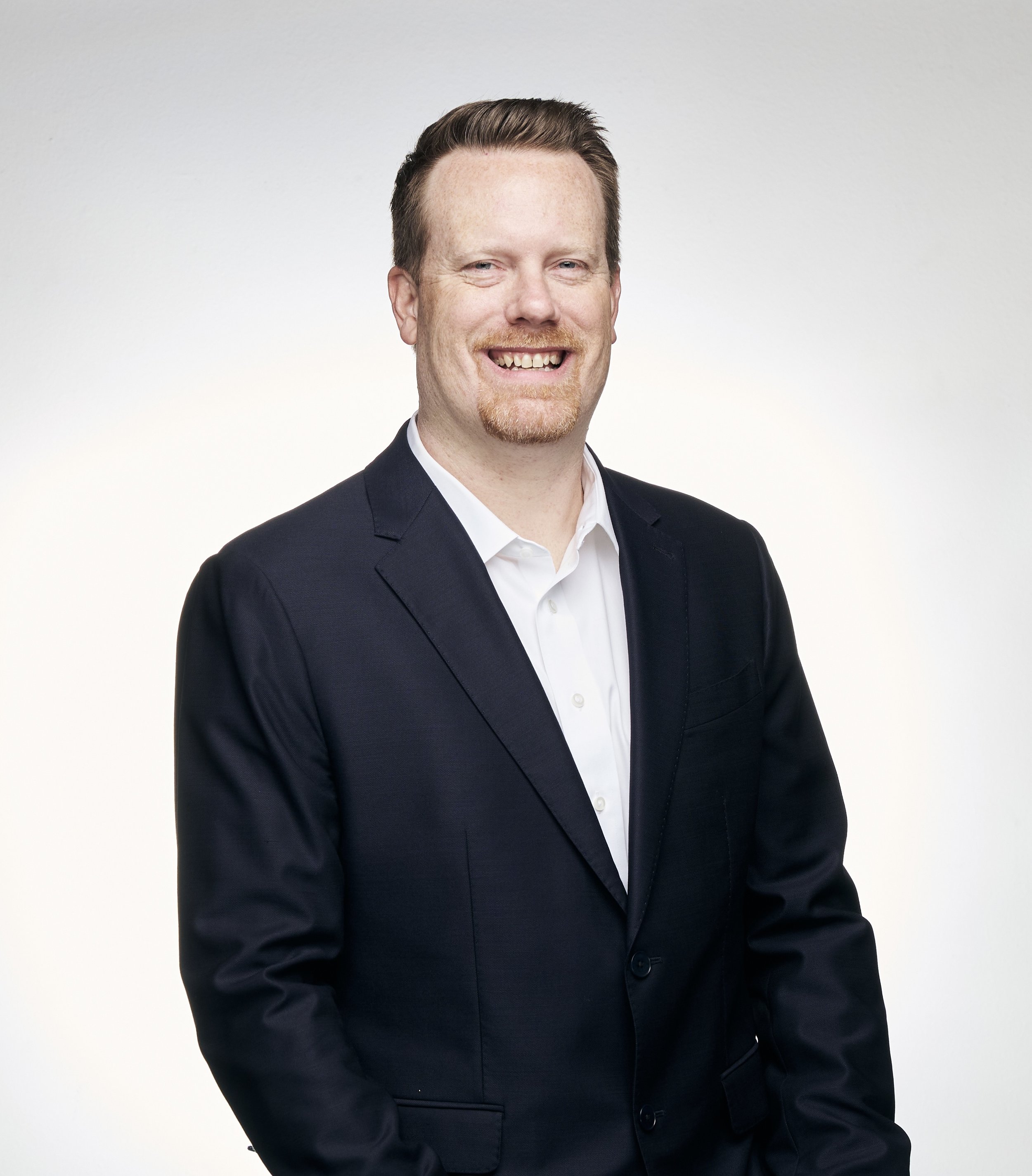 image of a man in a blue suit with short brown hair with a mustache and beard smiling