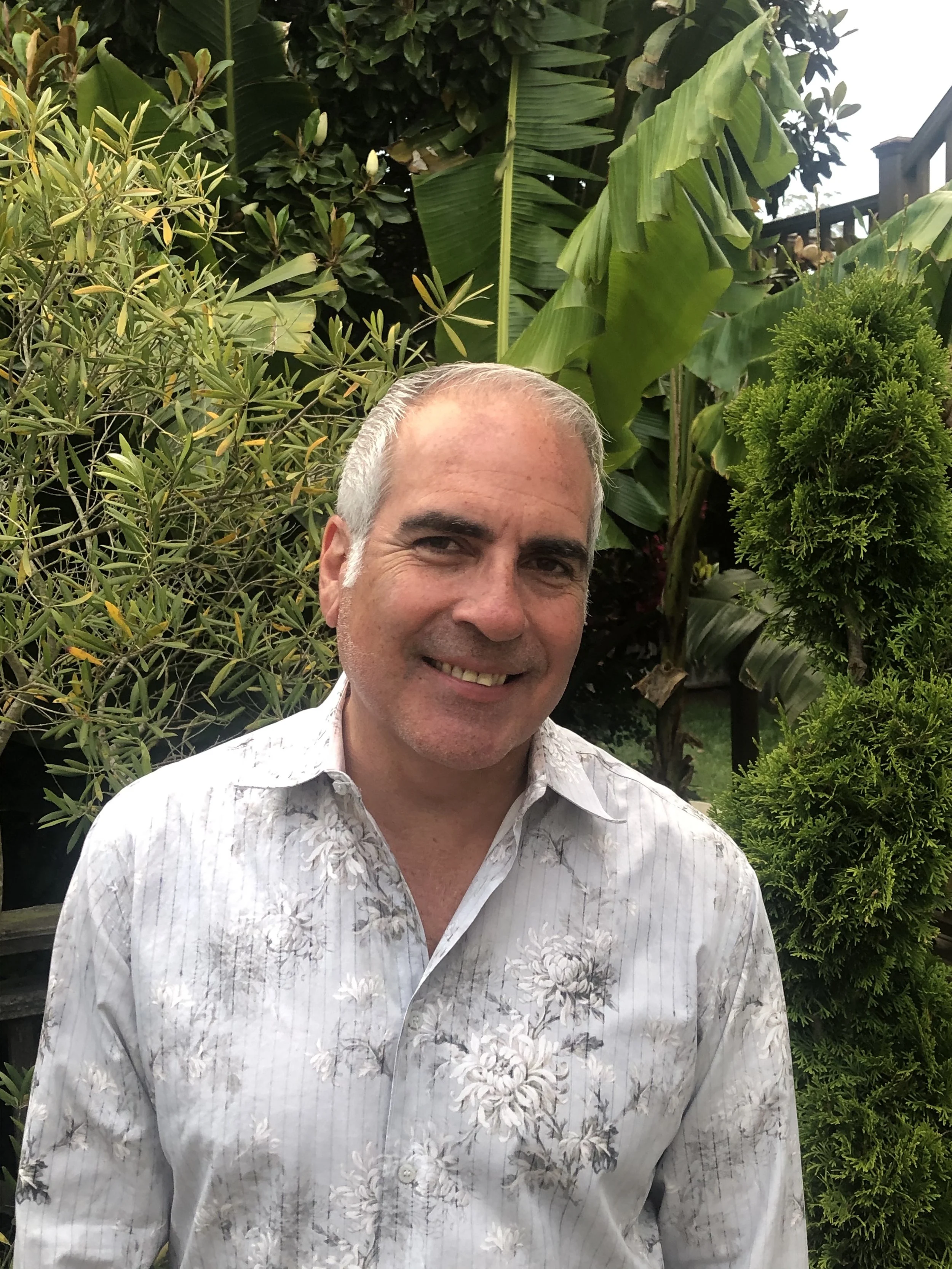 headshot of a man with grey hair and grey button down shirt smiling