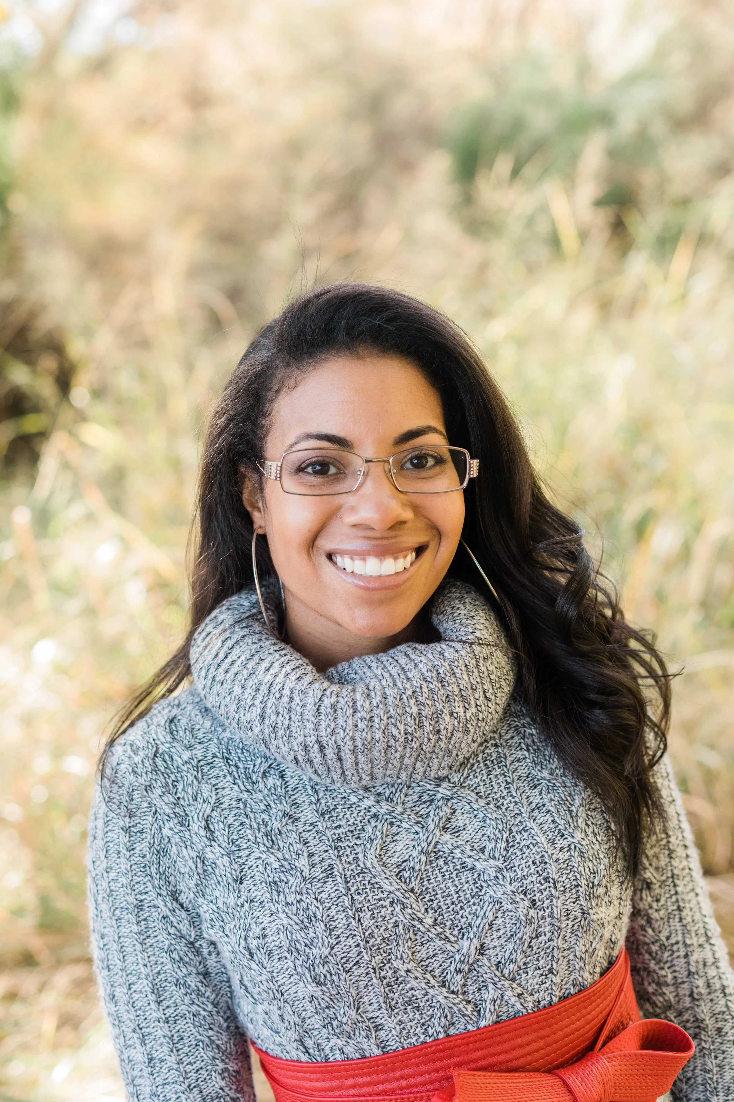 headshot of a woman with long dark hair wearing a grey sweater and glasses smiling