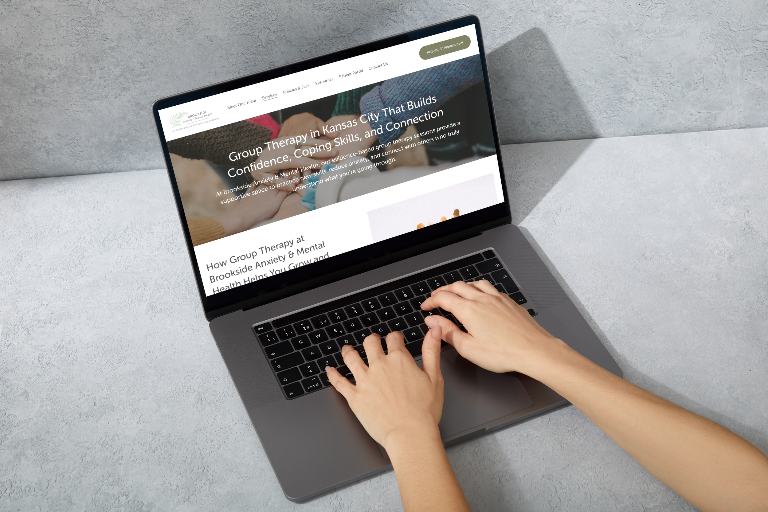 A person using a laptop on a textured gray surface, viewing a healthcare website about group therapy for anxiety and mental health.