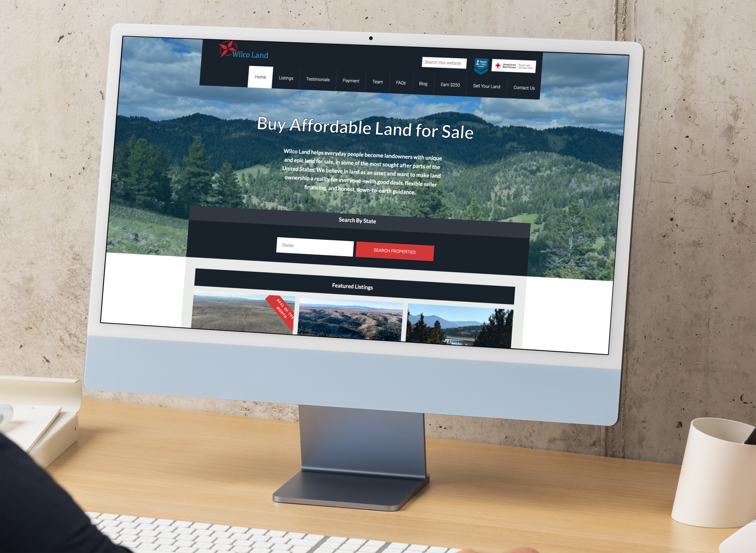 Computer monitor displaying a real estate website with a scenic mountain background and options to search for land for sale.