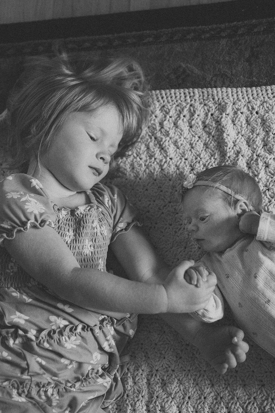 A toddler and infant sister hold hands