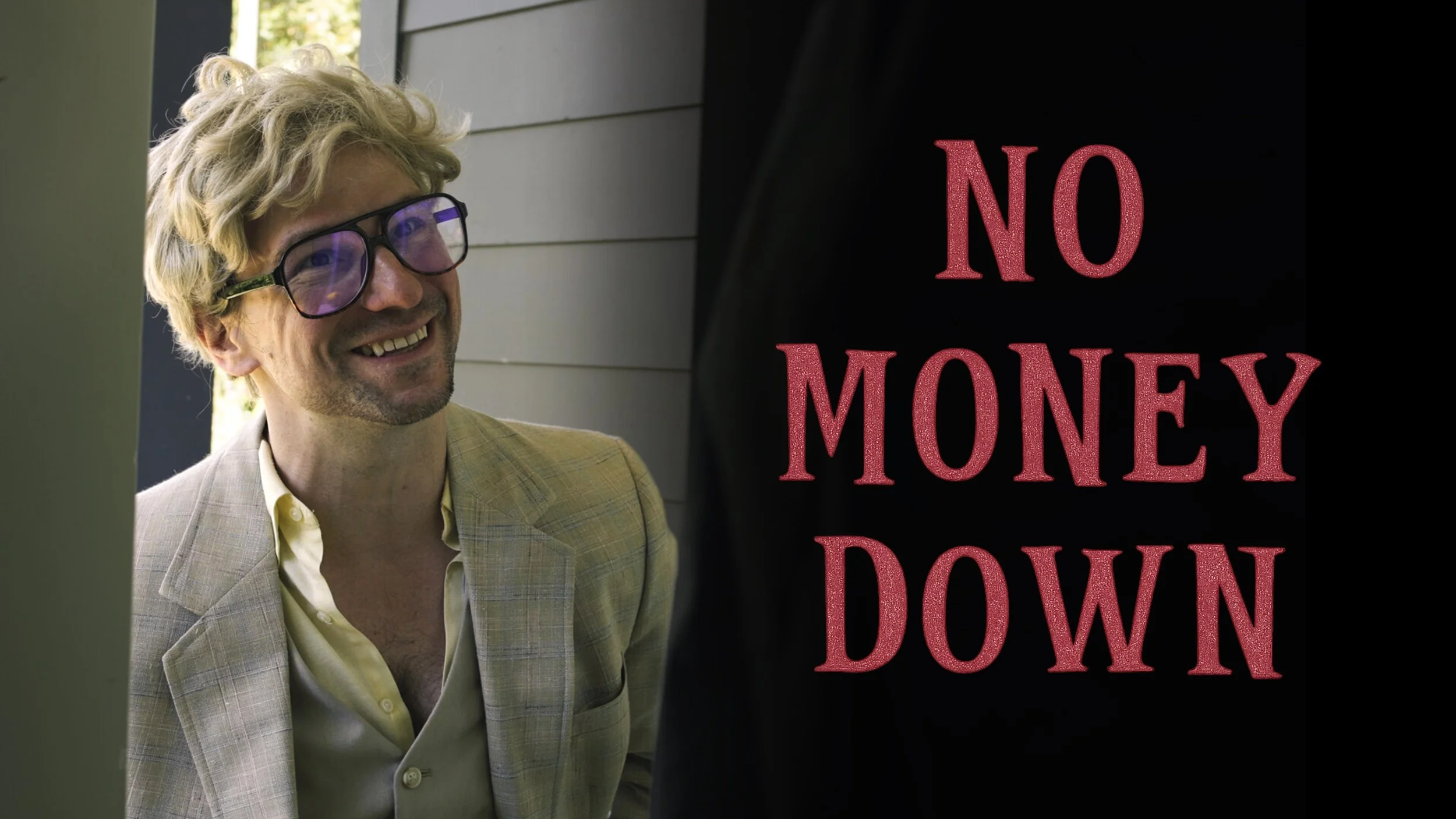 A man with blond hair, glasses, and a light-colored plaid suit smiling, standing by a window with trees outside, next to a black screen with red text that says 'NO MONEY DOWN'.