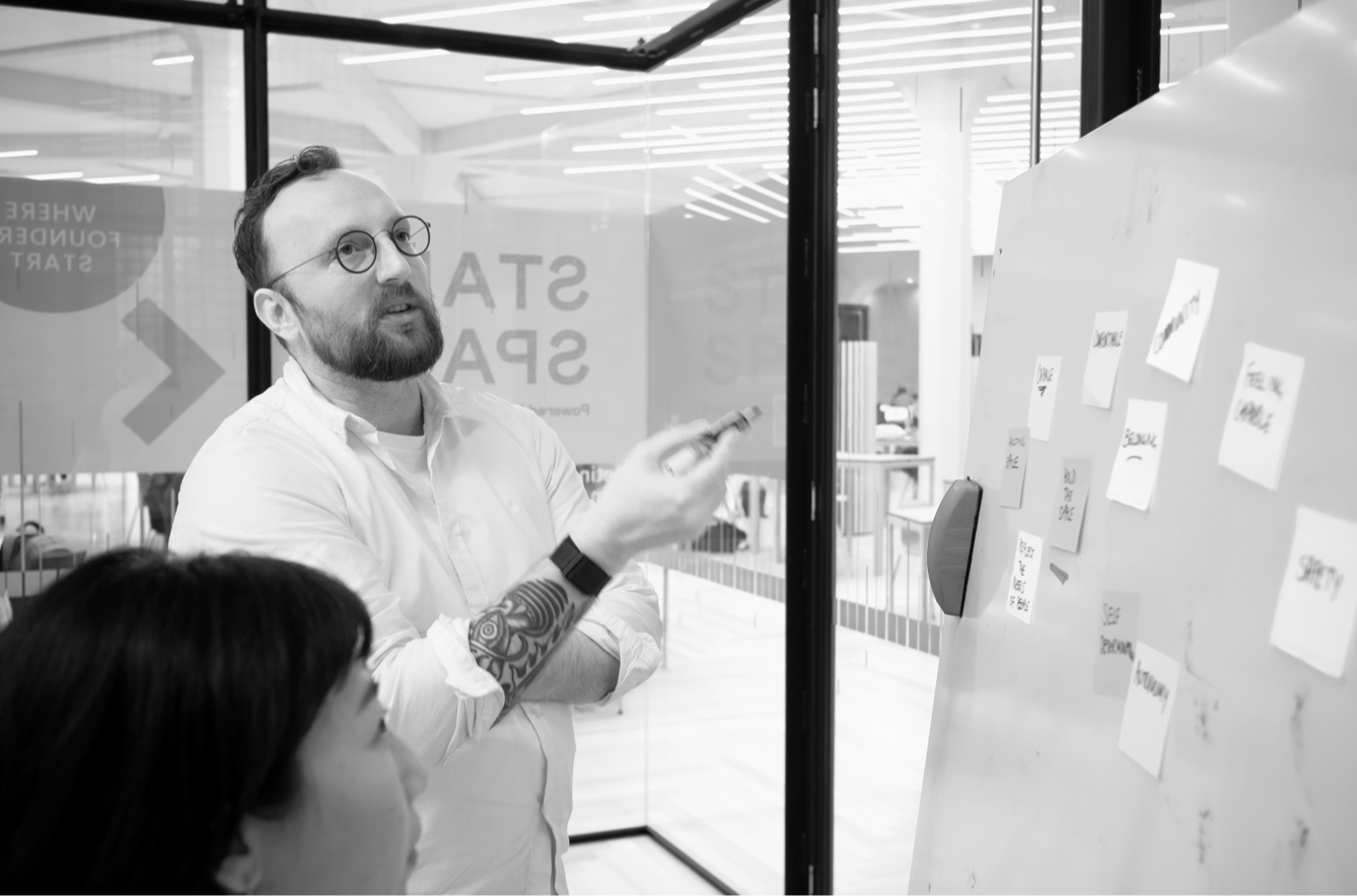 Man with glasses and woman work together on a white board