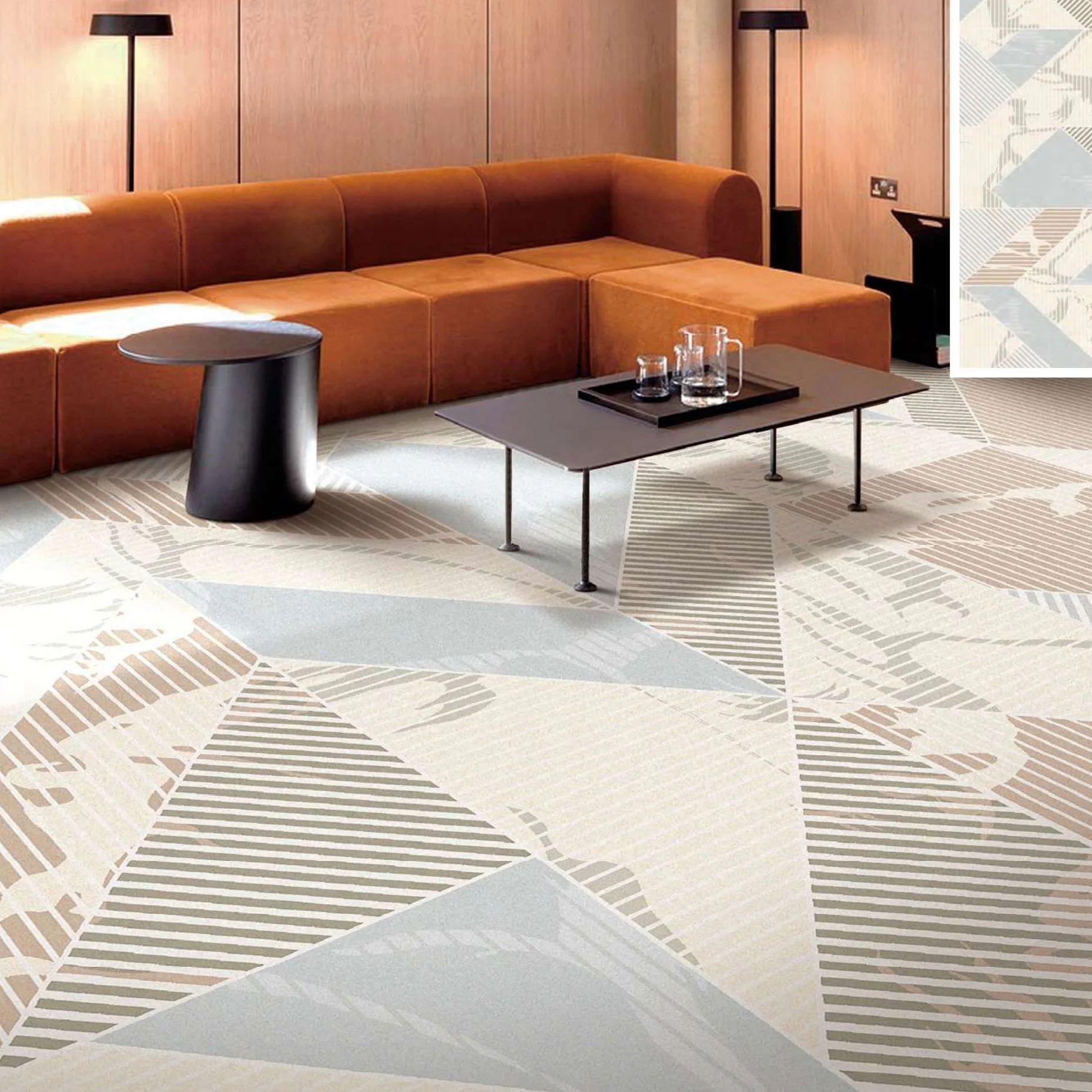 Axminster and Print Hospitality Modern hotel lounge with an orange sectional sofa, black side tables, a small black coffee table with glass pitchers and glasses, black floor lamps, wooden wall paneling, an electrical outlet, and patterned carpet.