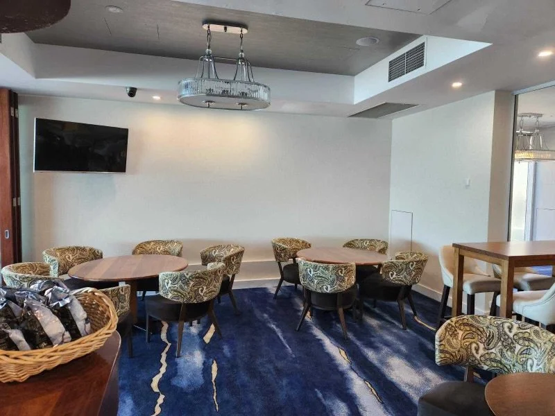Axminster and Print Hospitality Carpets - suitable to pubs, clubs, hotels, bars:  A modern lounge or meeting area with round tables and upholstered chairs, a chandelier, a wall-mounted TV, and a large blue patterned carpet.