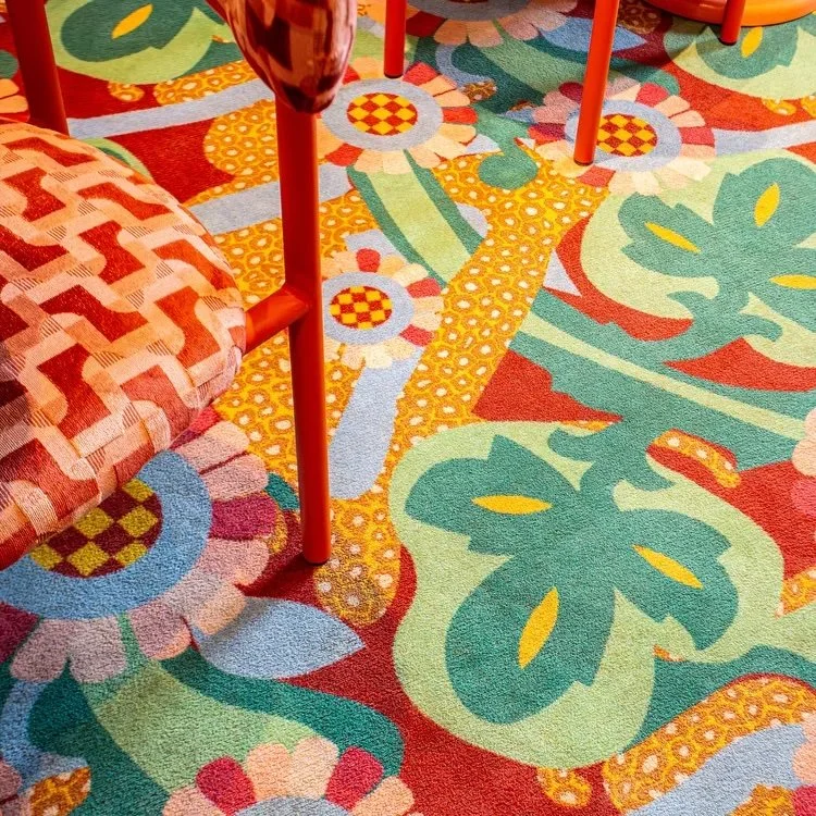 Axminster and Print Hospitality Carpets - suitable to pubs, clubs, hotels, bars: : Colorful patterned carpet featuring large green leaves, flowers, and geometric shapes, with part of an orange chair visible.
