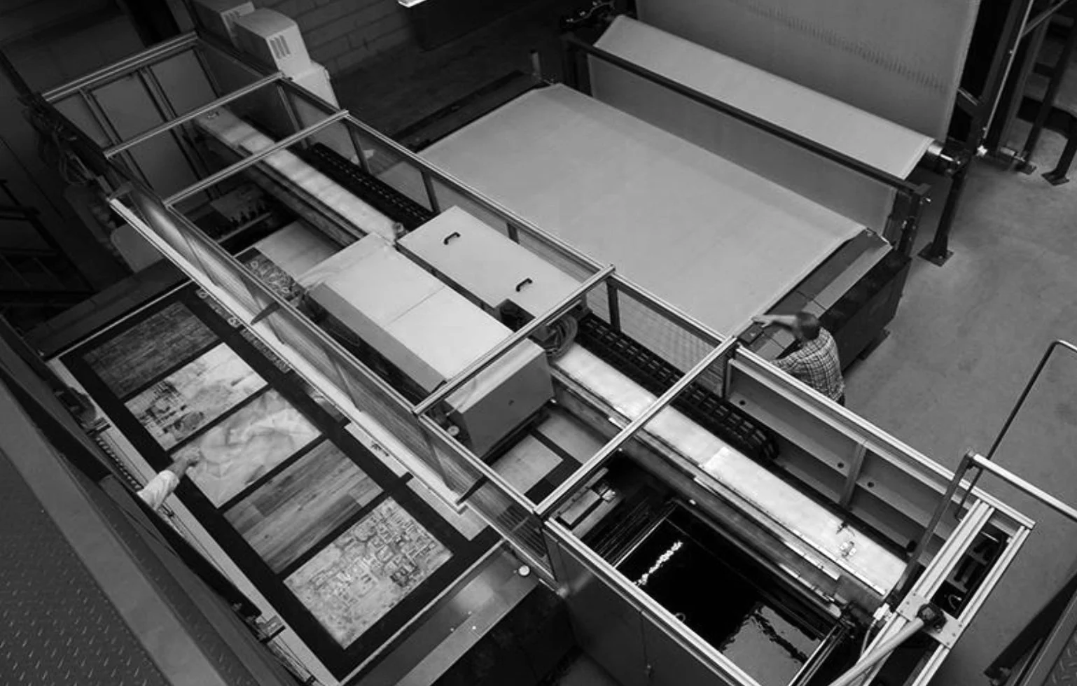 Axminster and Print Hospitality Carpets - suitable to pubs, clubs, hotels, bars:  Printing Carpet Machine Black and white photo of a conveyor belt system in a printing or packaging facility, with a person standing nearby.