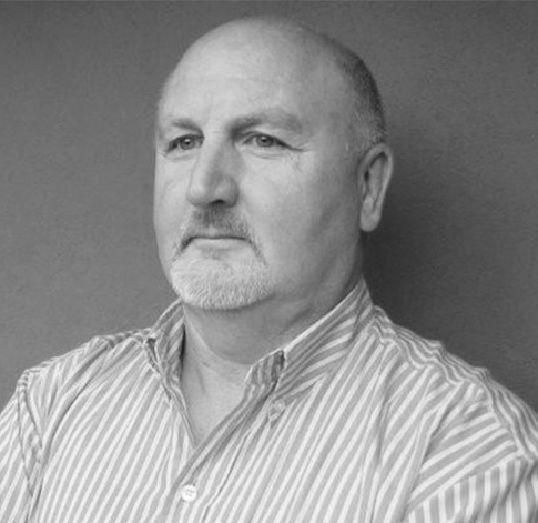 Black and white portrait of a middle-aged man with a serious expression, short hair, and a beard, wearing a striped button-up shirt.