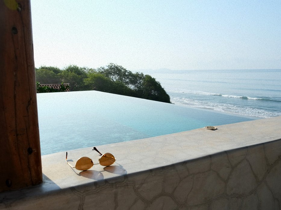 Sunglasses on a ledge overlooking an infinity pool and the ocean beyond on a clear day.