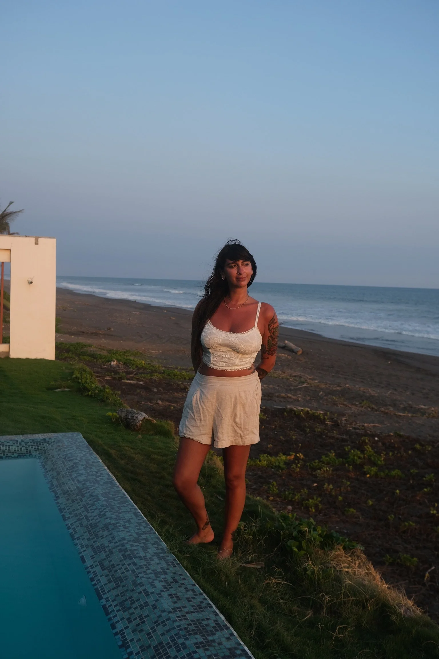 A woman standing on a grassy area near a beach with ocean waves in the background.