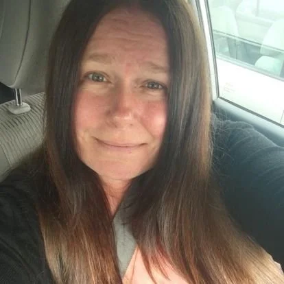 Person with long brown hair sitting in a car.