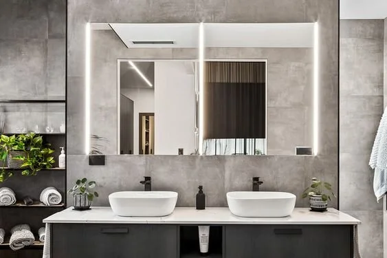 Close-up of a double vanity with large bathroom mirrors illuminated by vertical lights on both sides.