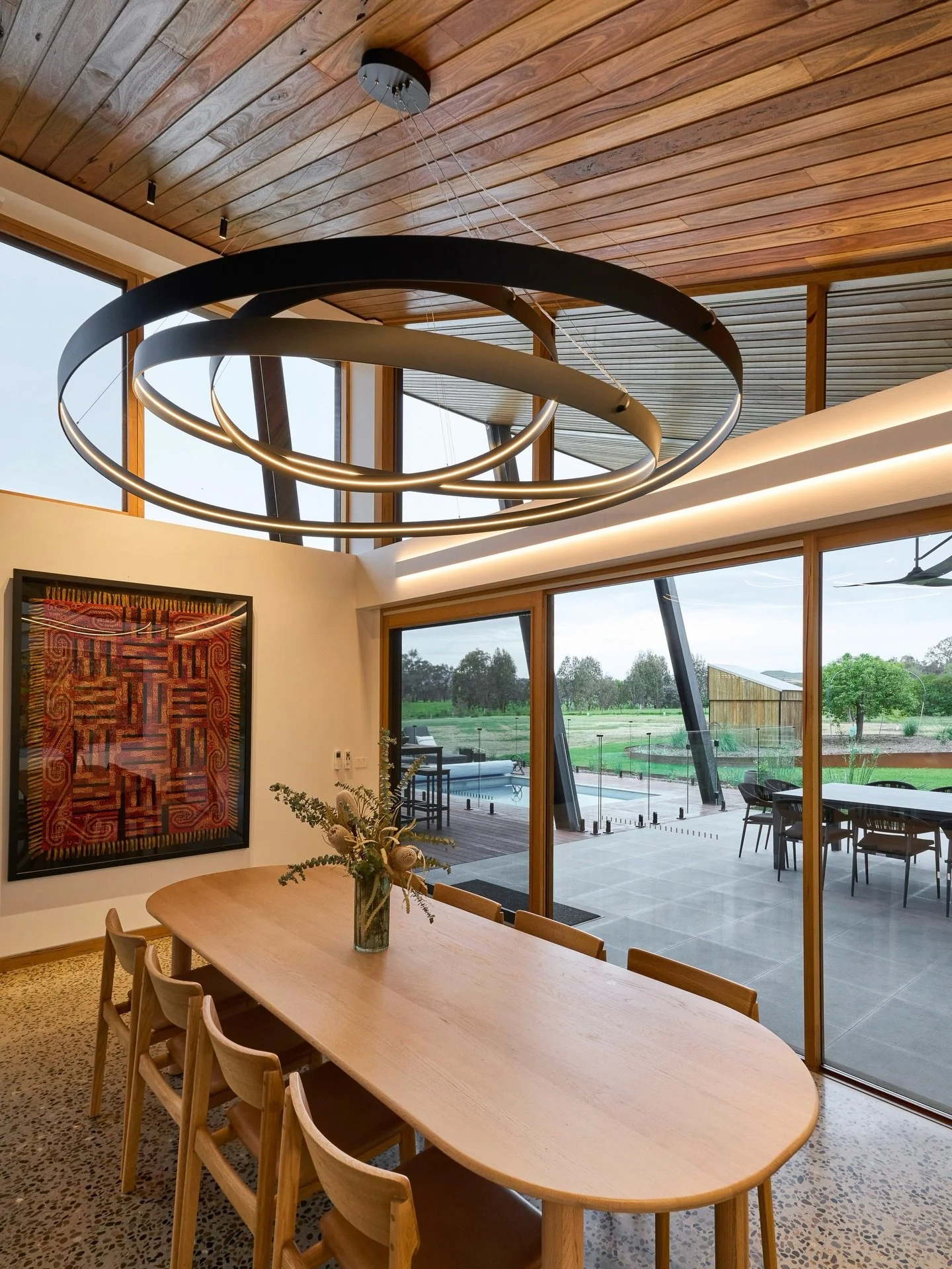 The grand circular pendant, positioned above the dining area, serves as a striking focal point. Designed and custom-fabricated specifically for this home, its outer ring spans an impressive three metres in diameter, while dramatic lighting is achieve