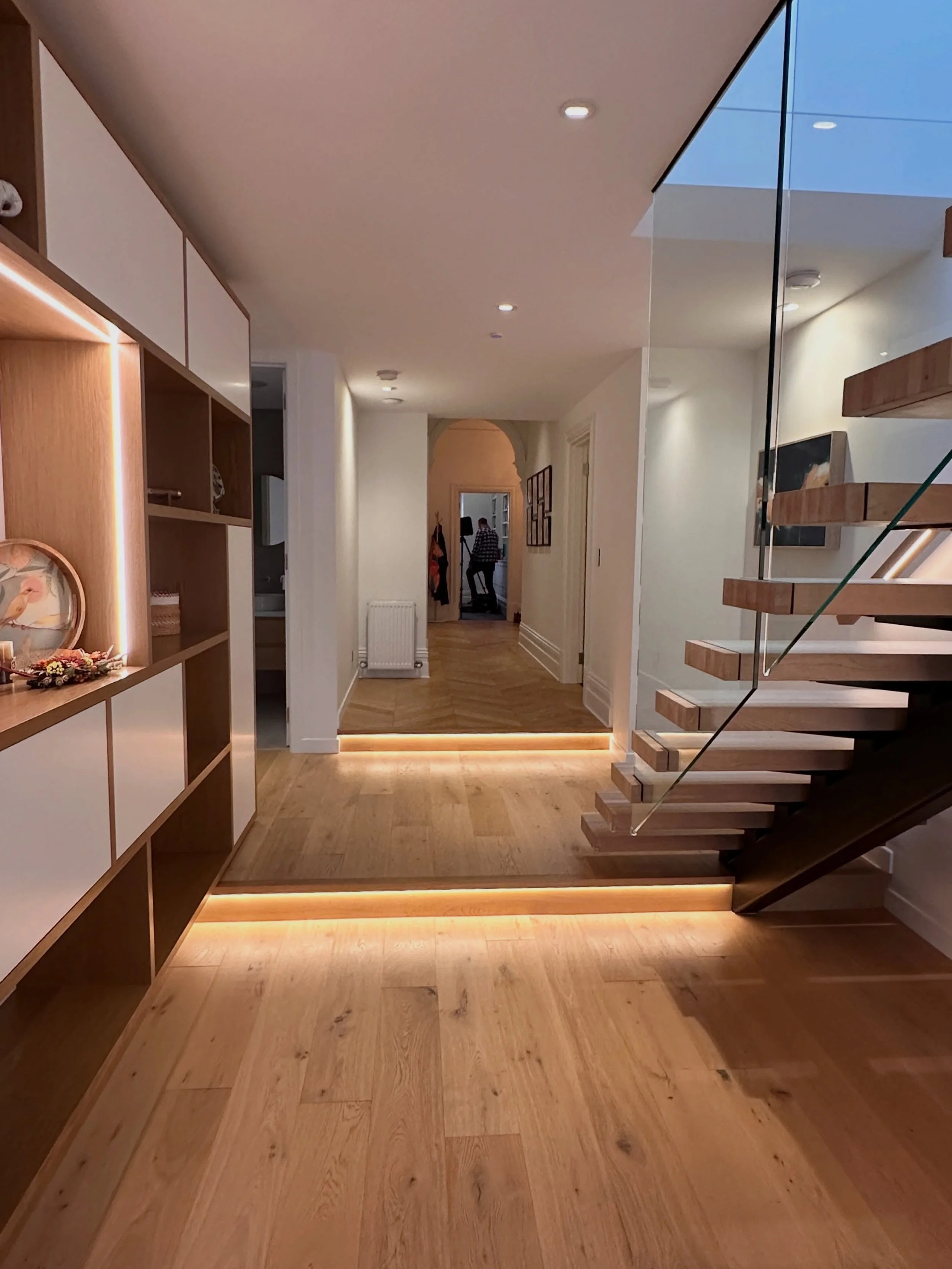 As you move from the front entry and the heritage part of the home, the hallway becomes a threshold where contemporary lighting begins to bridge the two eras. 

Light is concealed within the stair handrails, the open shelving joinery, and the transit