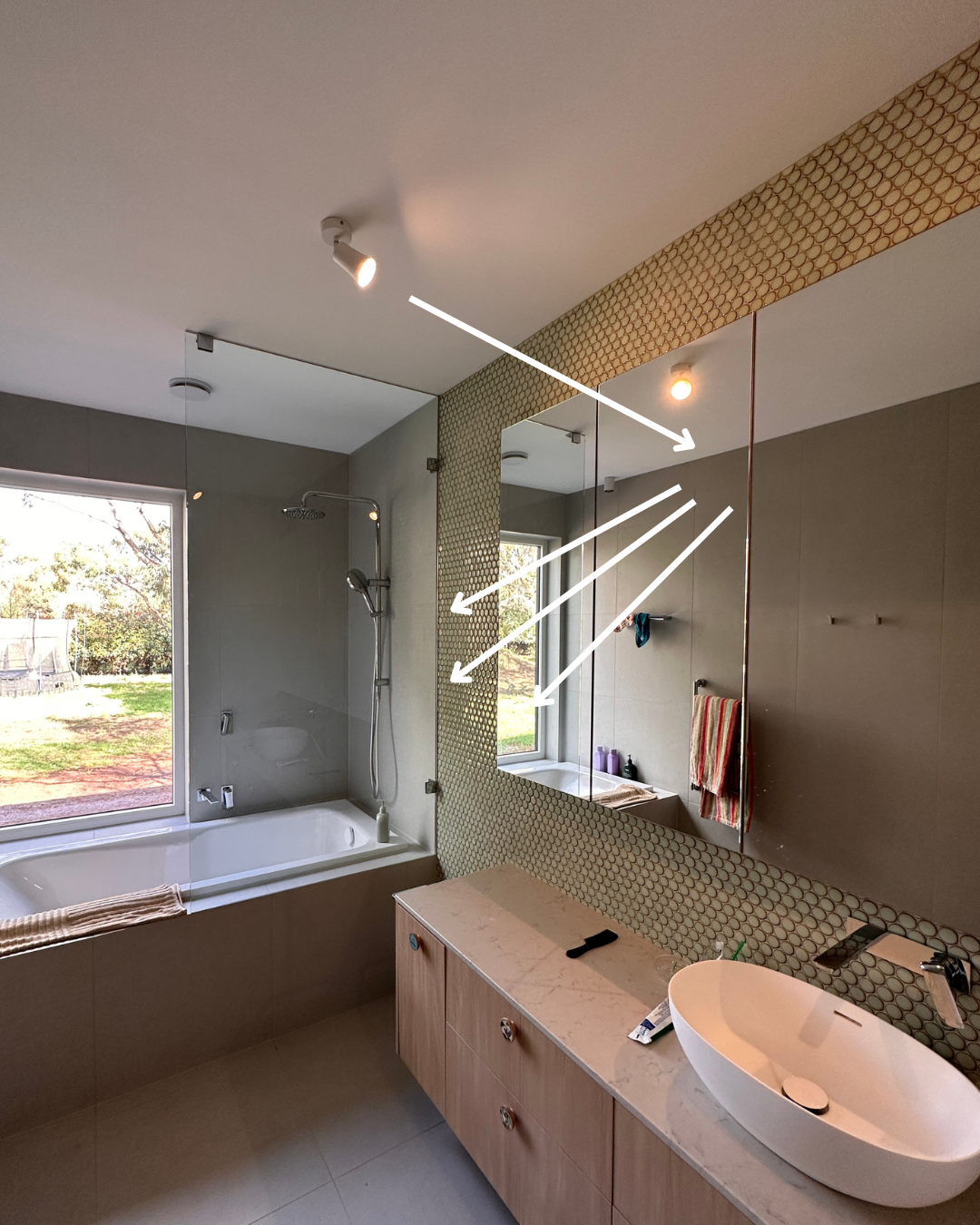 Woodend bathroom mirror reflecting adjustable ceiling spotlights aimed towards the vanity