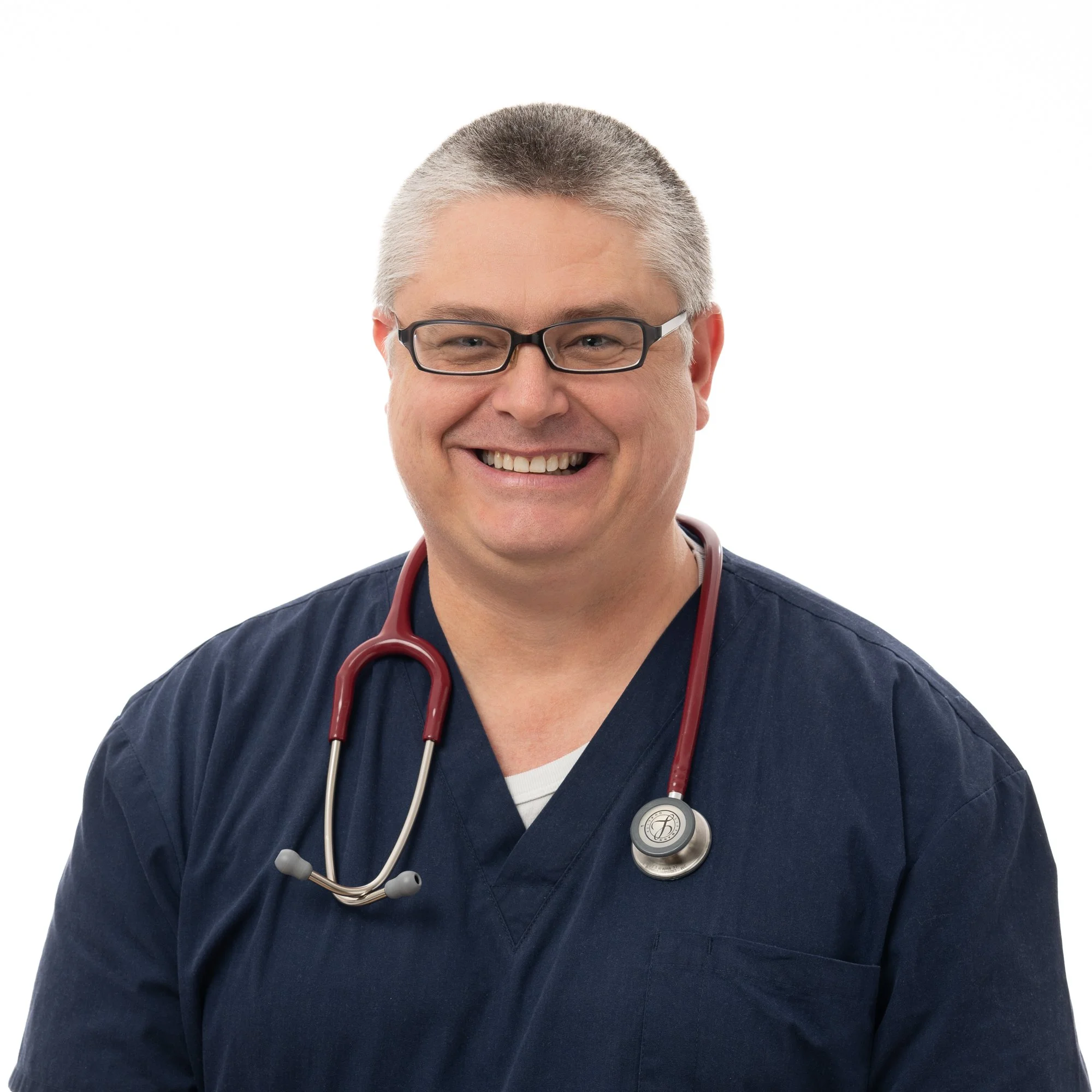 A smiling male healthcare professional with glasses, gray hair, wearing navy scrubs, and a red stethoscope around his neck.