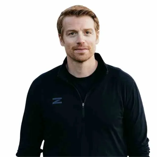 A client from Filim corp - Doug Lynch. A man with light skin, red hair, and a beard wearing a black jacket standing against a white background.