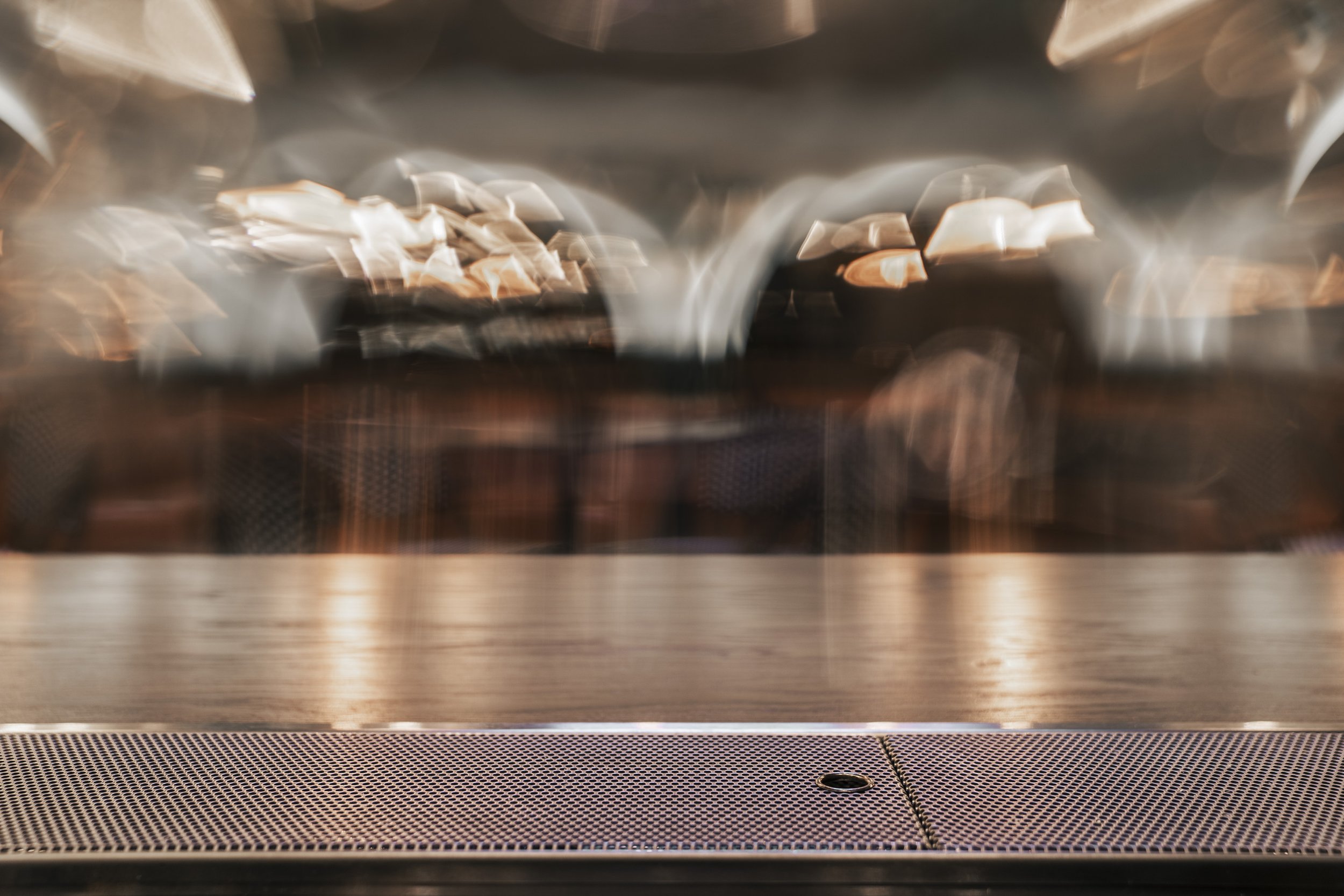 Blurry image of a metallic commercial oven or stove top with a glass cover, reflecting the kitchen lighting above. Restaurant build by Foundry Kitchens in Vancouver.