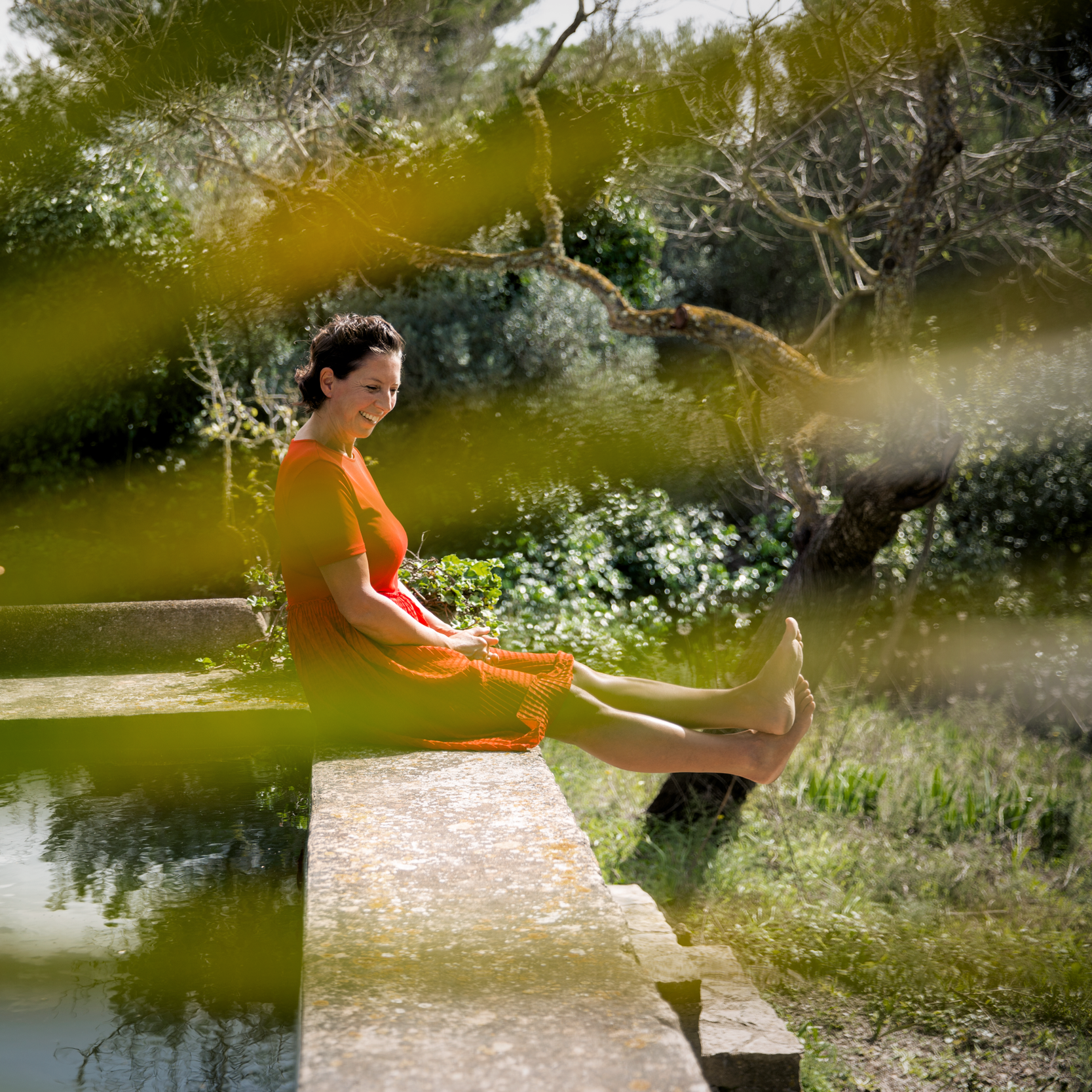 Marianne laughing while sitting on the edge of a stone water trough in a Mallorca garden